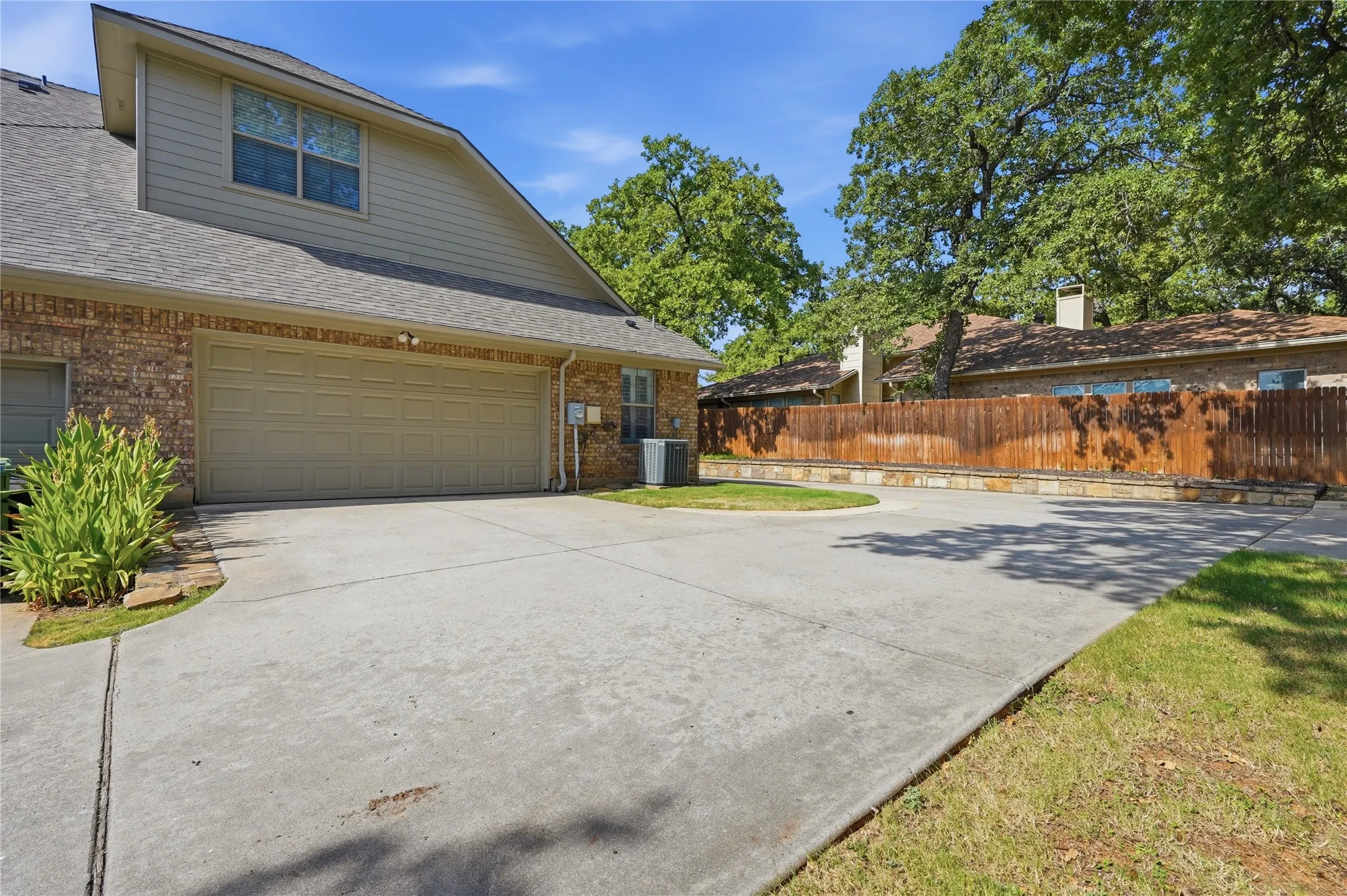 Brick exterior featuring an attached two-car garage, concrete driveway, and mature landscaping