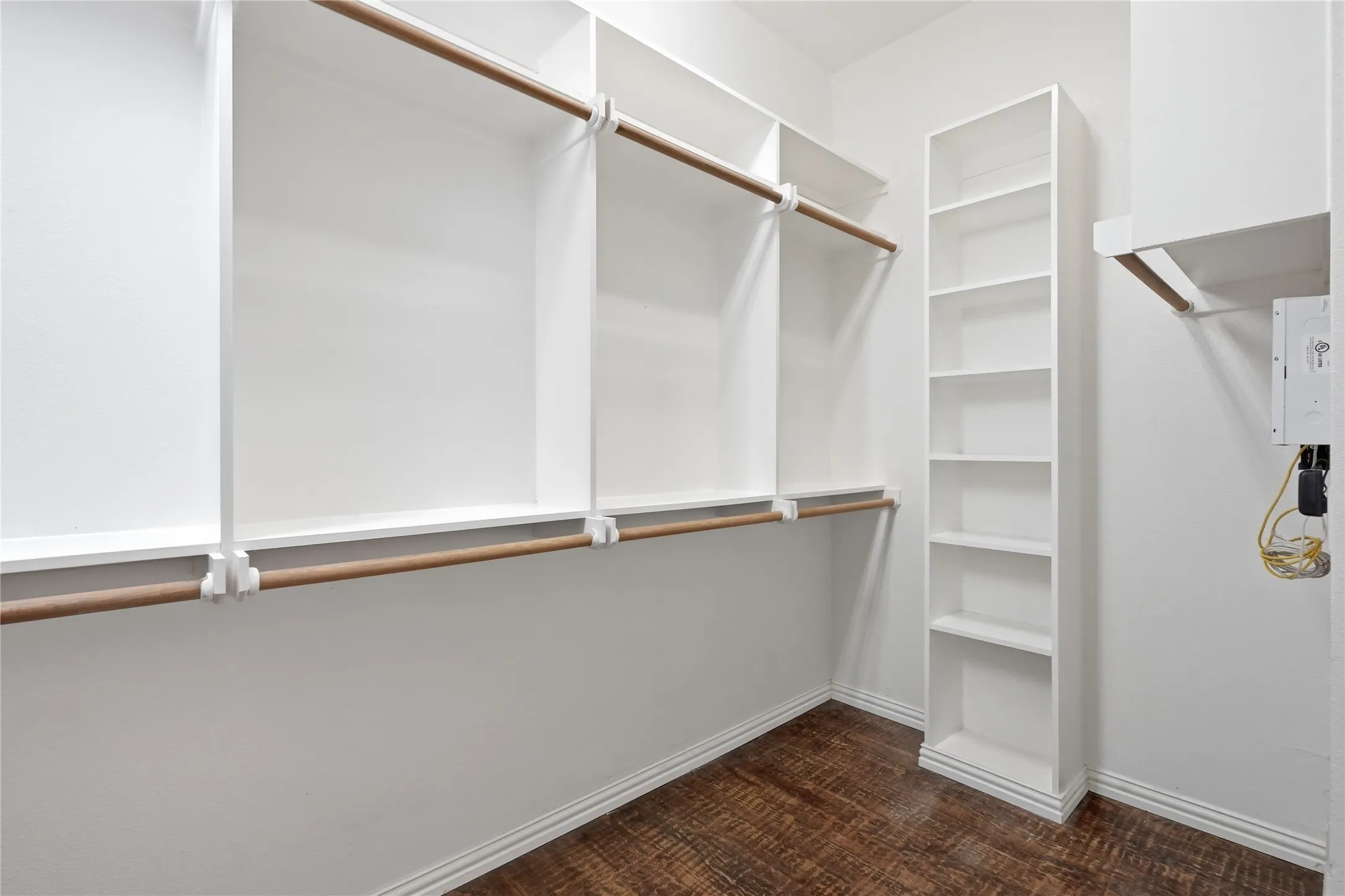 Walk-in closet featuring built-in white shelving, wood-finish flooring, and white baseboards