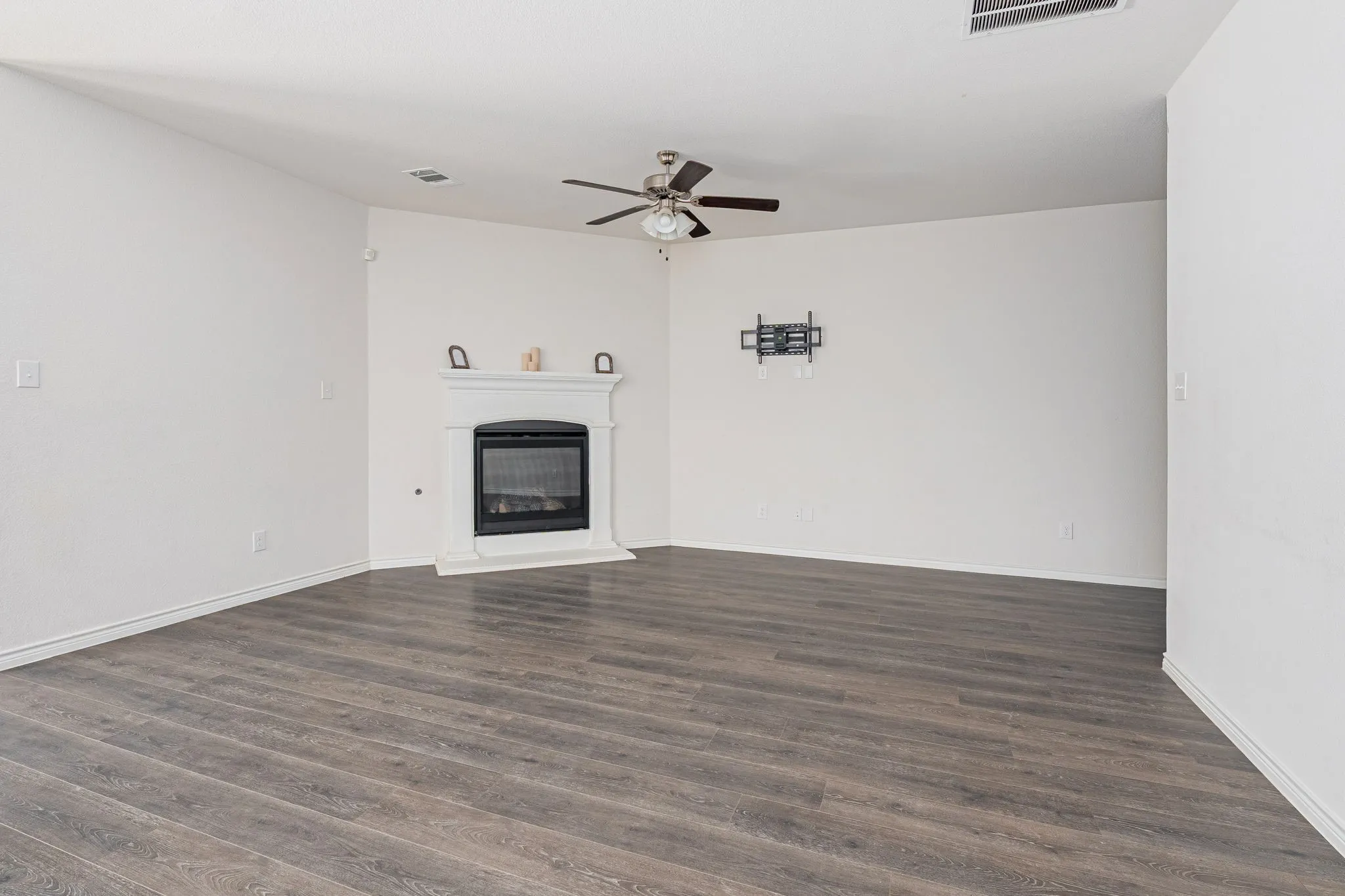 Unfurnished living room with ceiling fan, dark wood-style flooring, and a glass covered fireplace