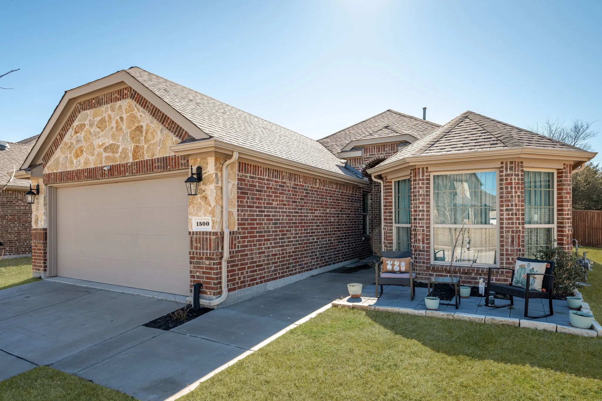 Single story home with brick siding, roof with shingles, concrete driveway, and a front lawn