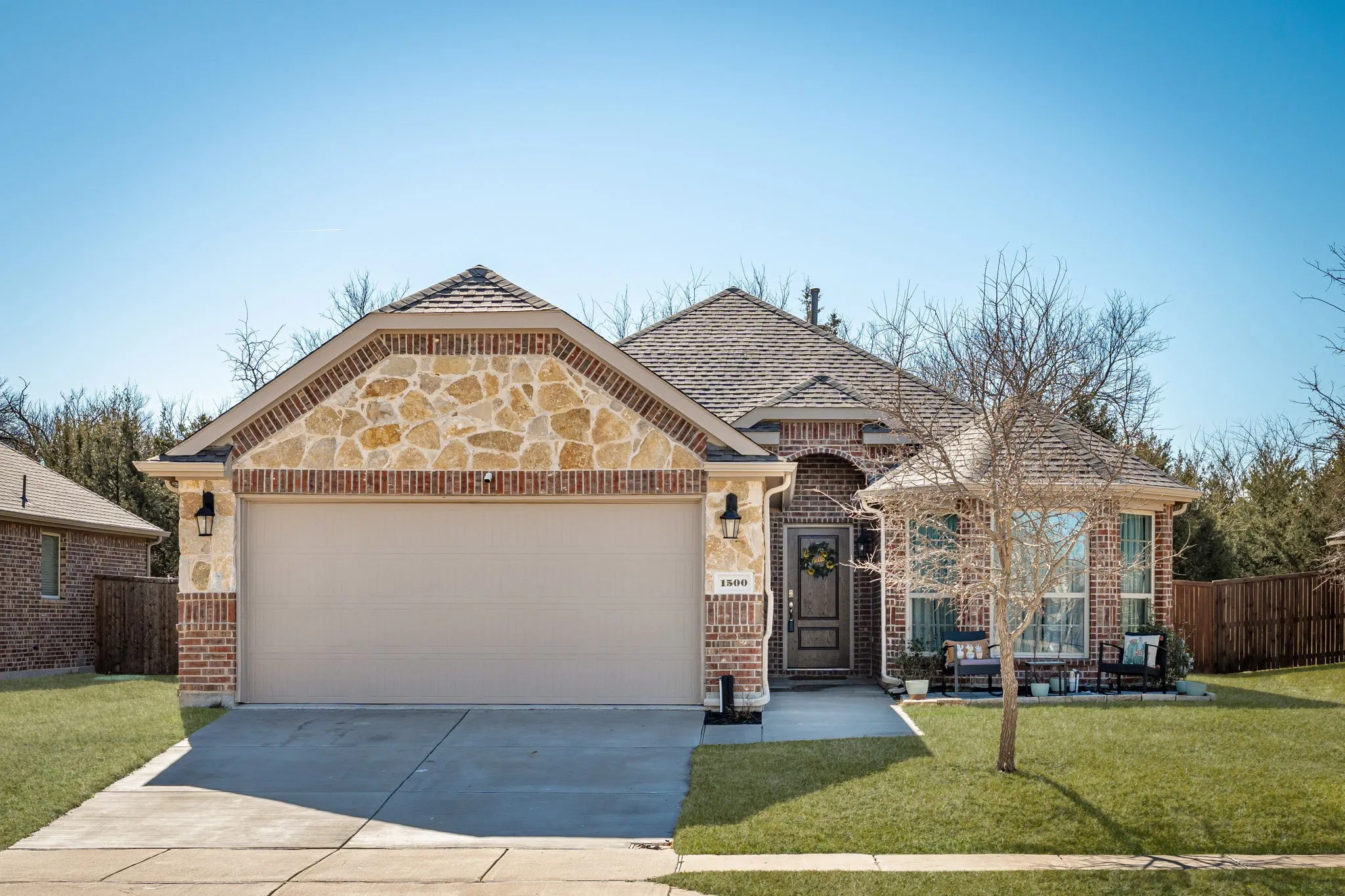 French country inspired facade featuring brick siding, concrete driveway, an attached garage, and stone siding