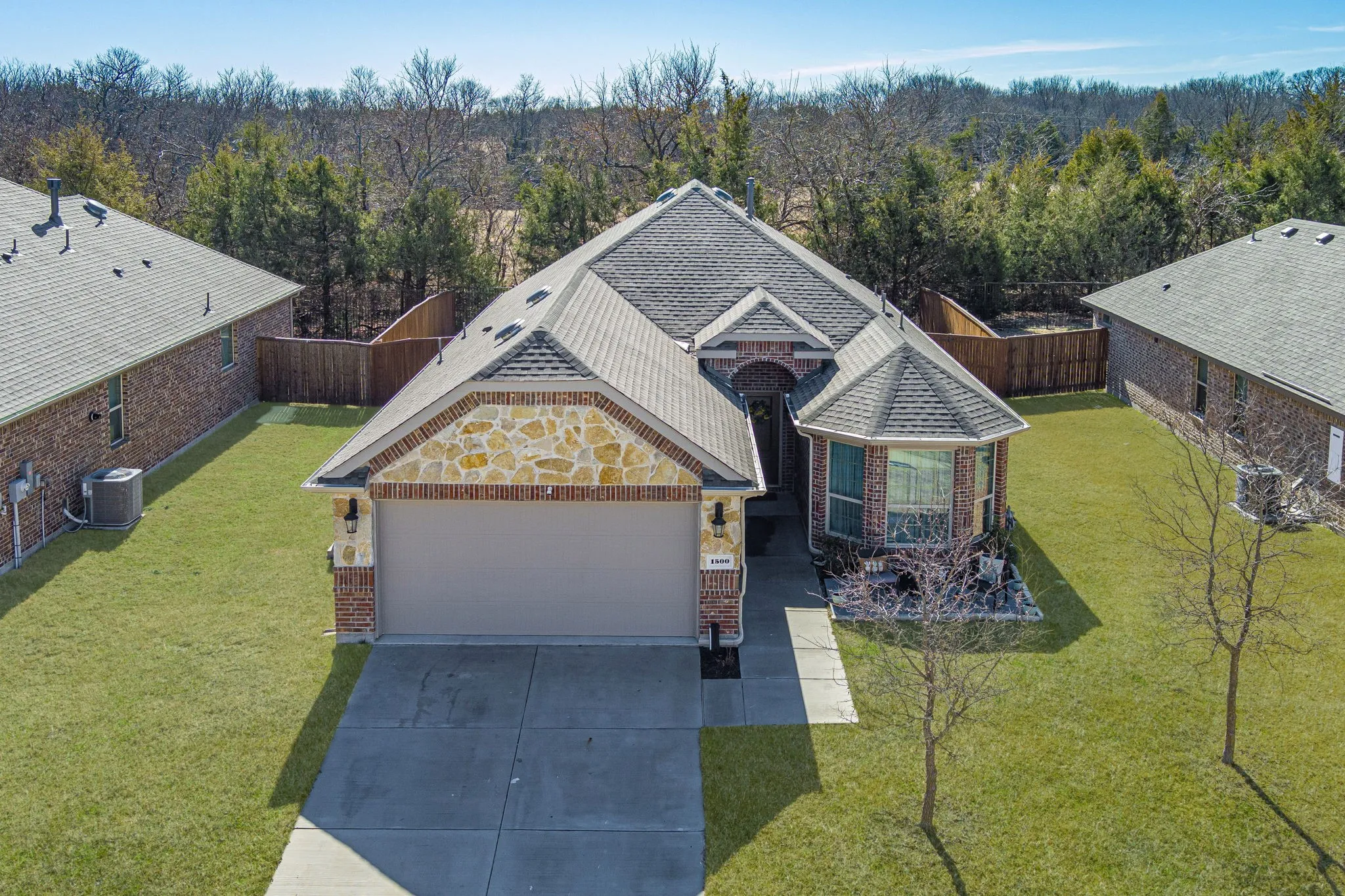 View of front of home featuring concrete driveway, an attached garage, brick siding, and a view of trees