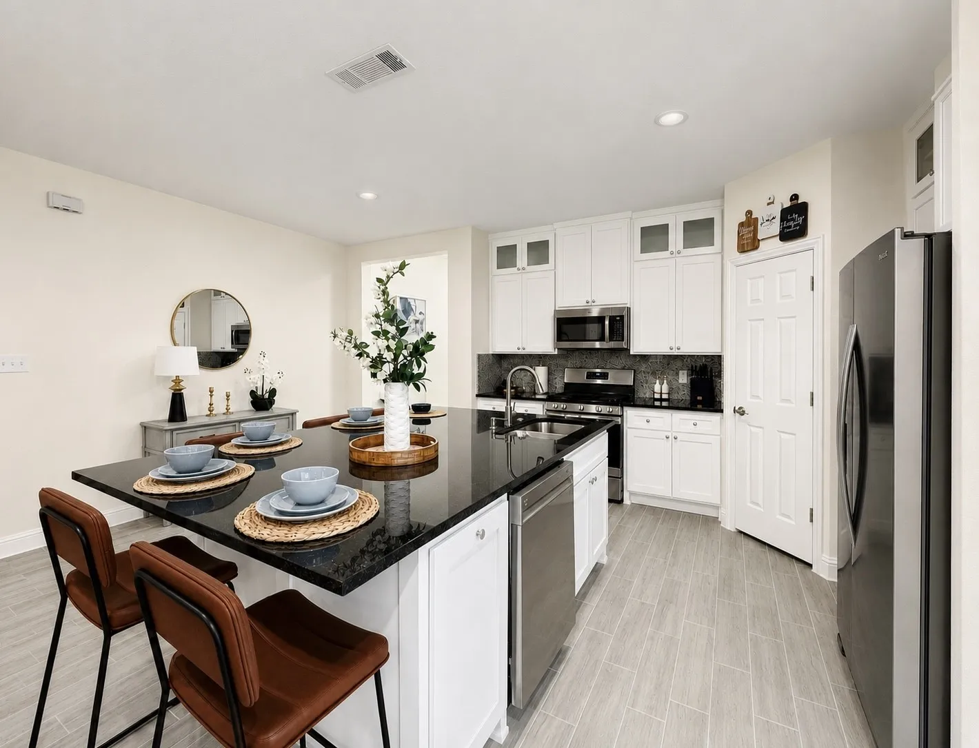 Modern kitchen featuring a large island with a dark countertop, white cabinetry, stainless steel appliances, and light wood-finish flooring