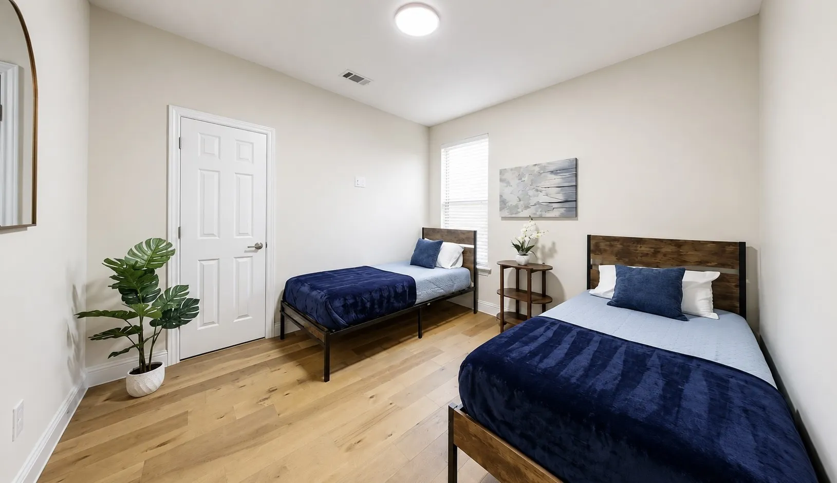 Bright bedroom featuring light wood-finish flooring, neutral wall tones, a white paneled door, and a white window blind