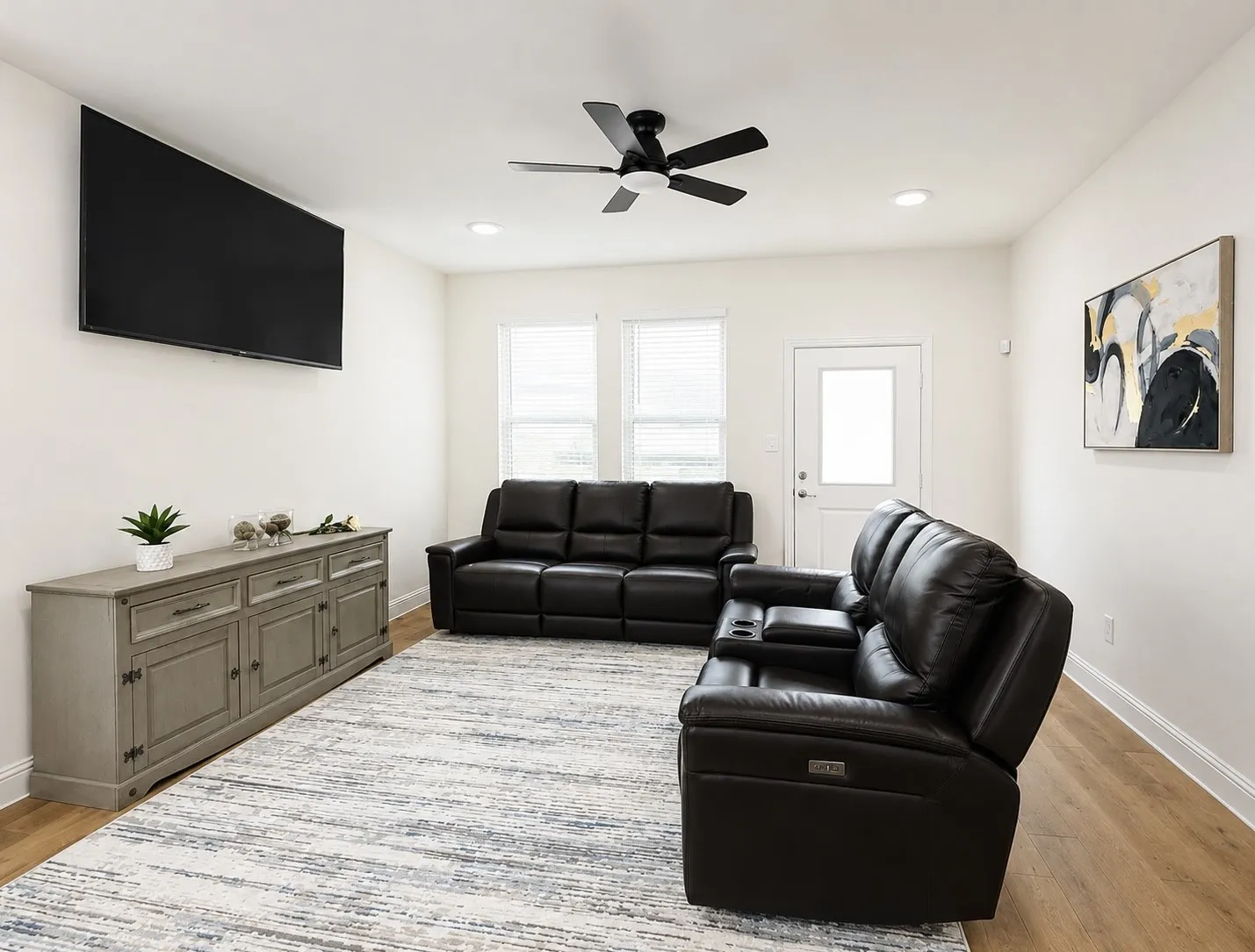 Spacious living area featuring light wood-finish flooring, a contemporary black ceiling fan with integrated lighting, and recessed ceiling lights