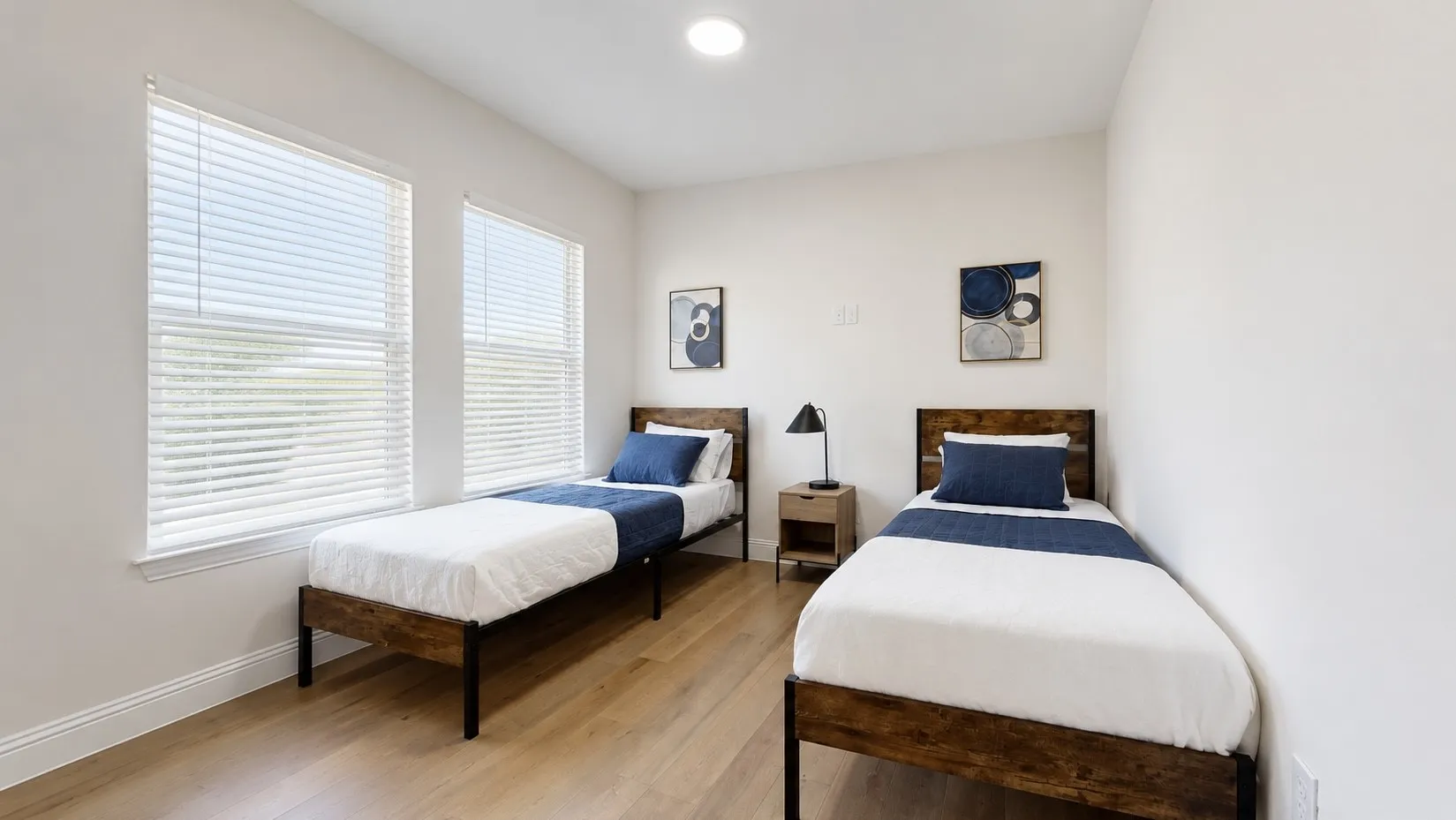 Room featuring two separate bed frames with wood-finish headboards, light wood-finish flooring, and white walls