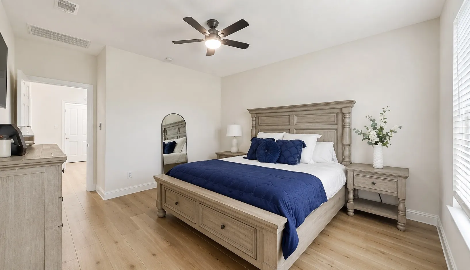 Spacious bedroom featuring light wood-finish flooring, a ceiling fan with integrated lighting, and neutral wall tones