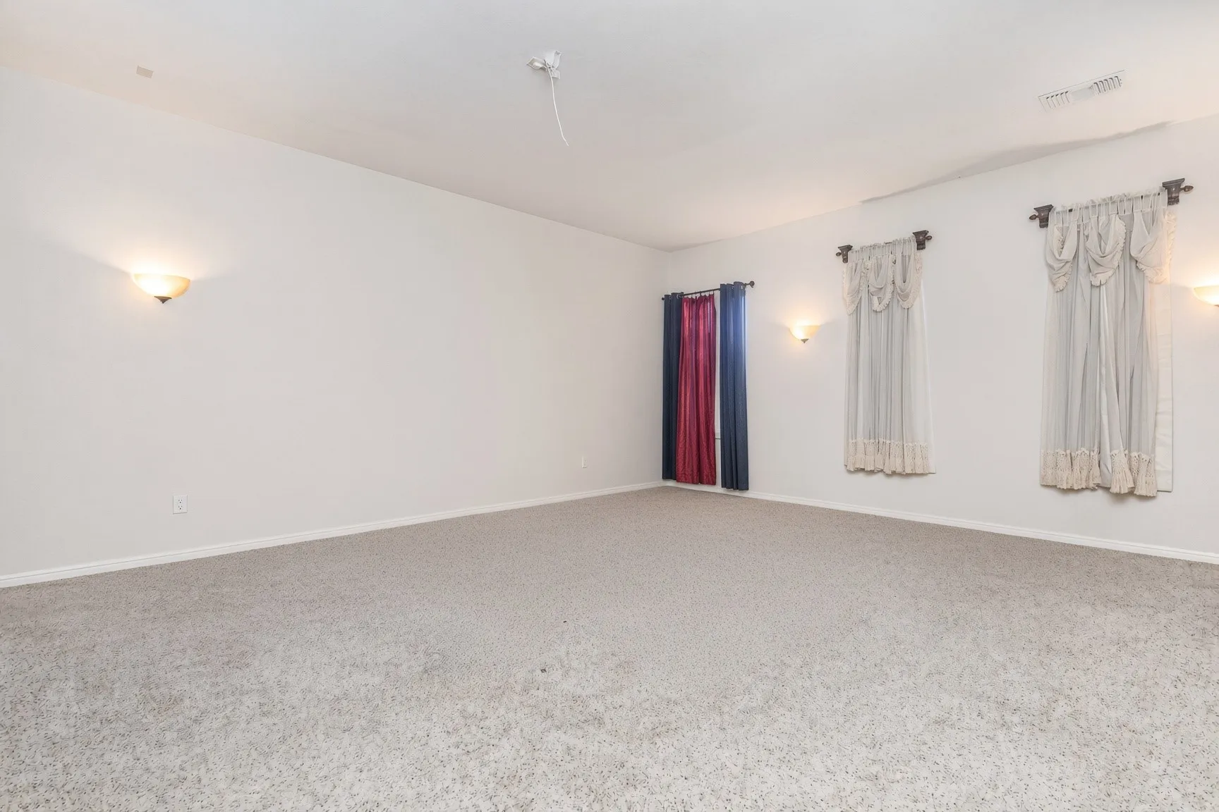 Spacious room with light-colored carpeting, multiple windows, and wall sconce lighting