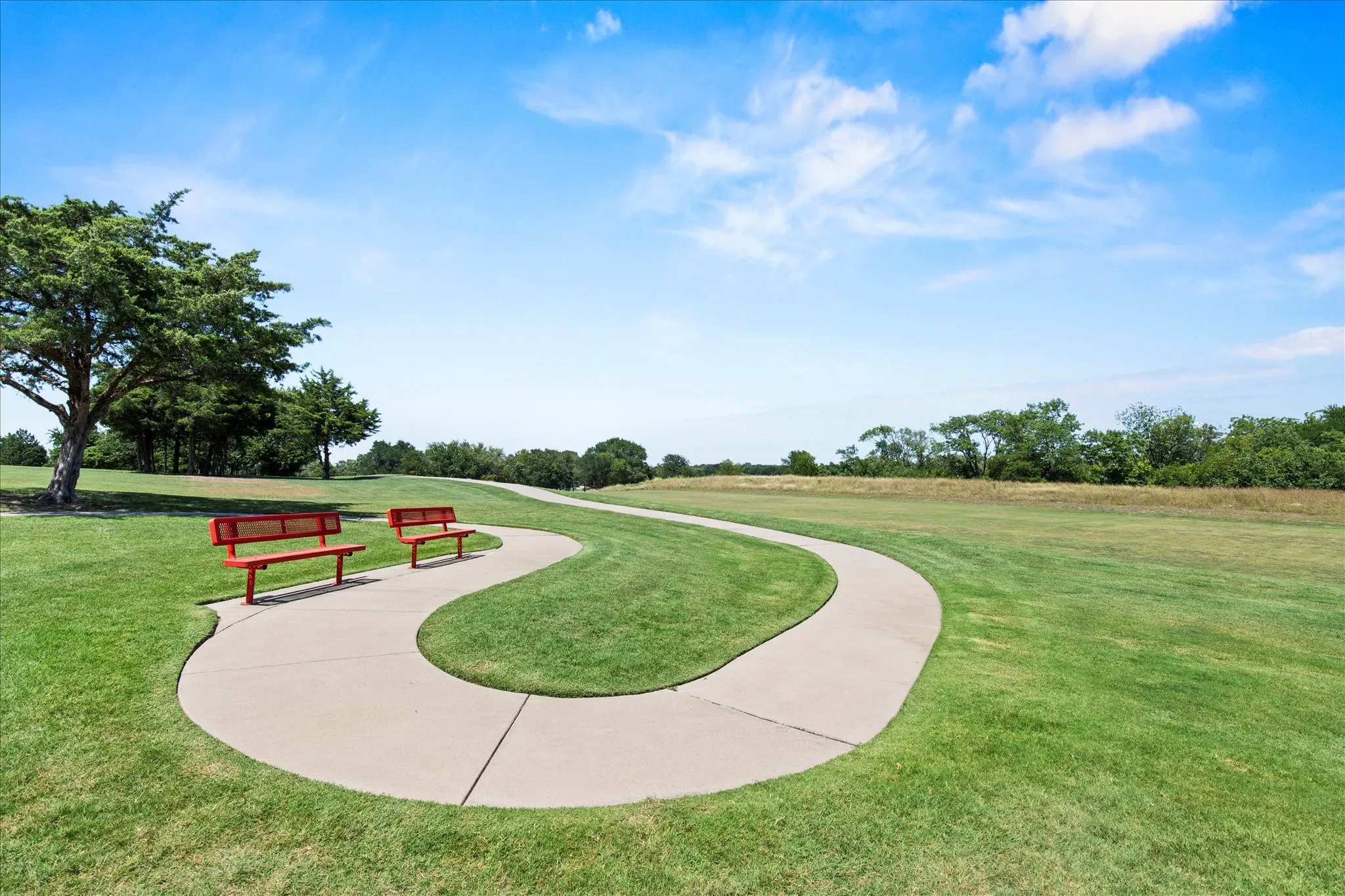 Curved concrete path winding through expansive green lawn, flanked by two red park benches