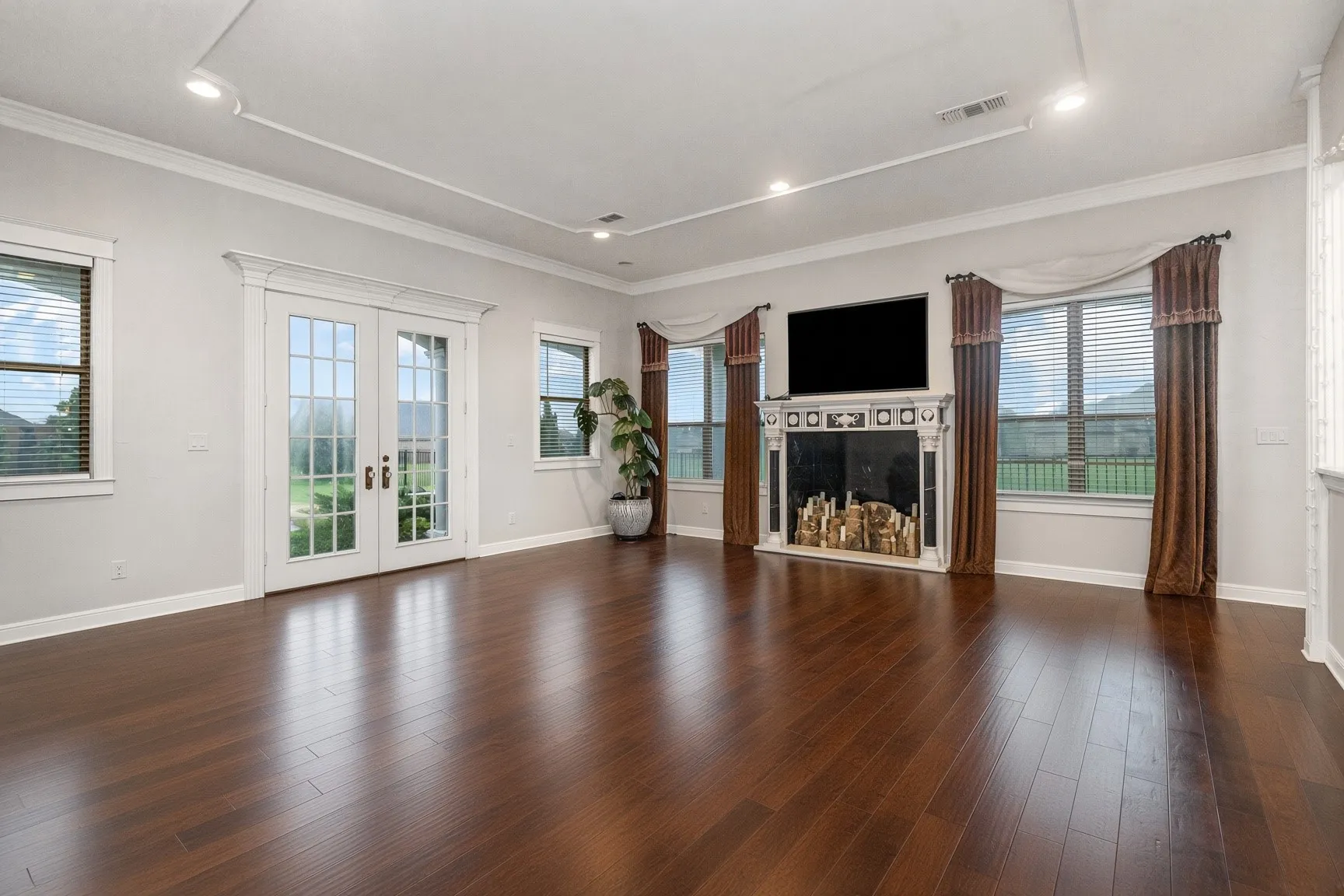 Hardwood-finish flooring, decorative fireplace, French doors, recessed lighting, and crown molding