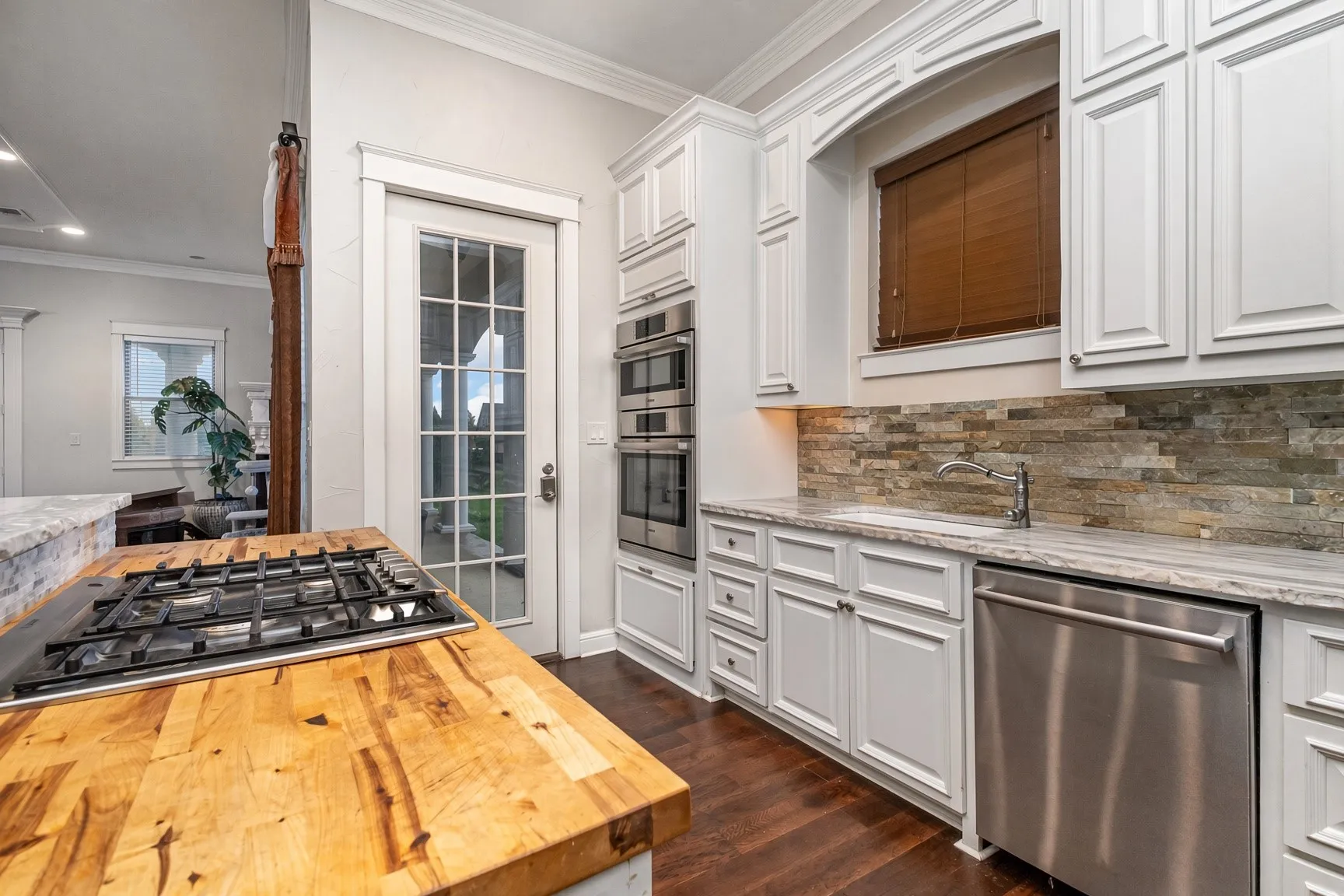 Built-in gas cooktop, wood-finish countertop, white cabinetry with crown molding, stainless steel built-in appliances, and a glass-paned door