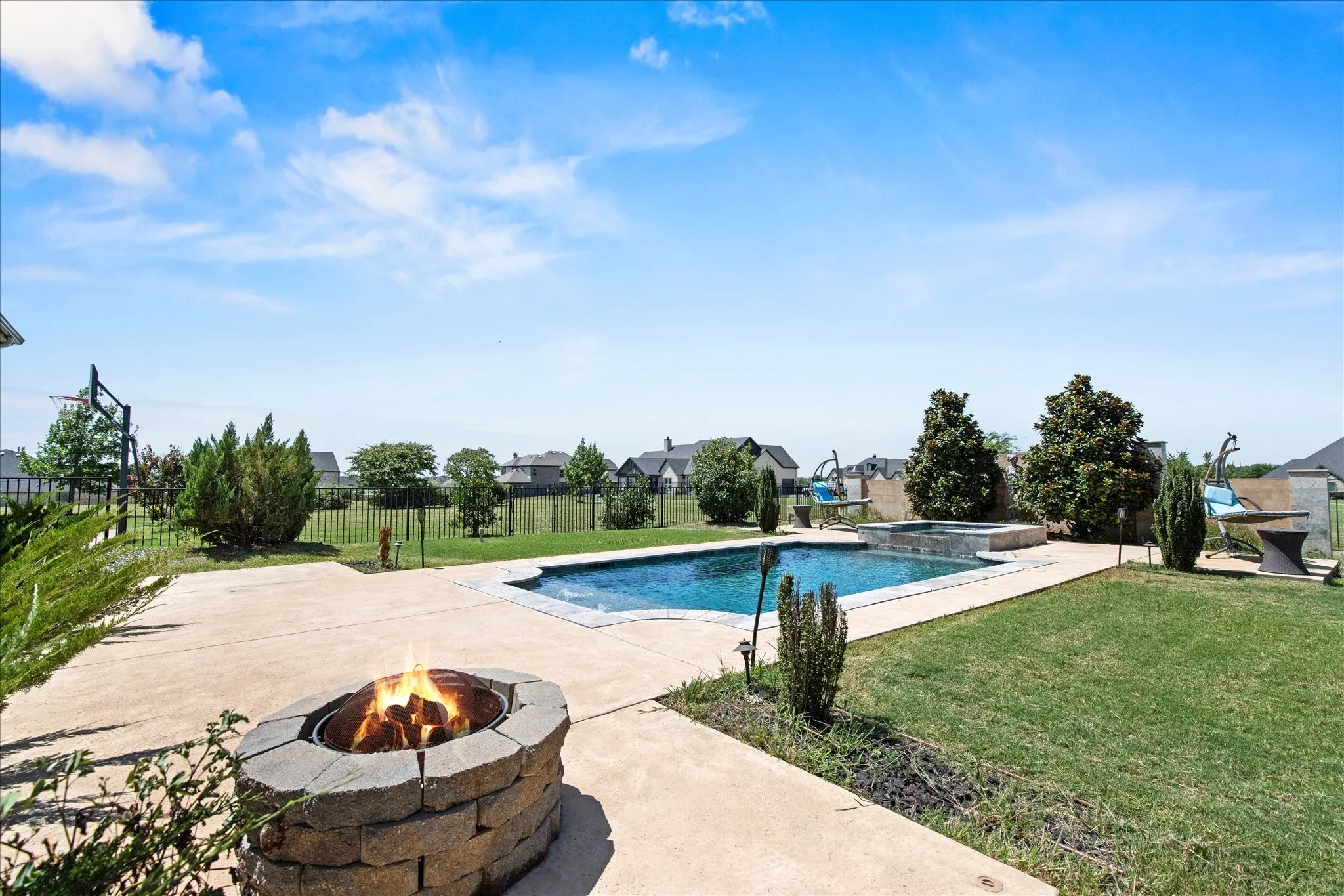 Expansive backyard oasis featuring a rectangular swimming pool, integrated spa, and a stone-clad fire pit