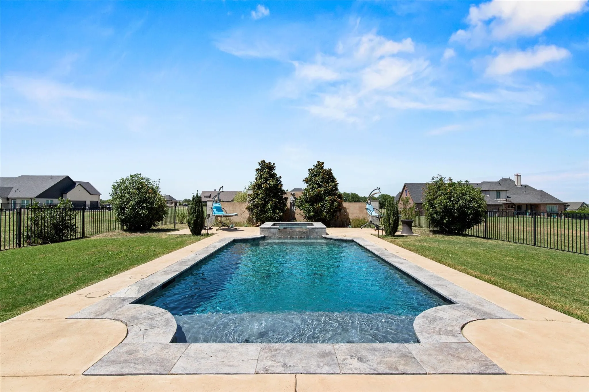 Rectangular swimming pool featuring a built-in spa, concrete decking, and stone coping