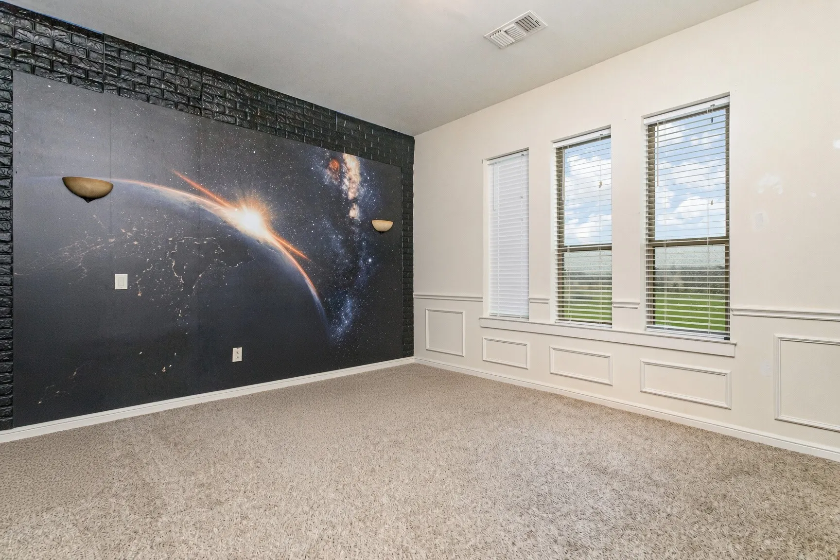 Wall-to-wall carpeting, three windows with horizontal blinds, decorative wainscoting, and a feature wall with a large-scale graphic and built-in sconces