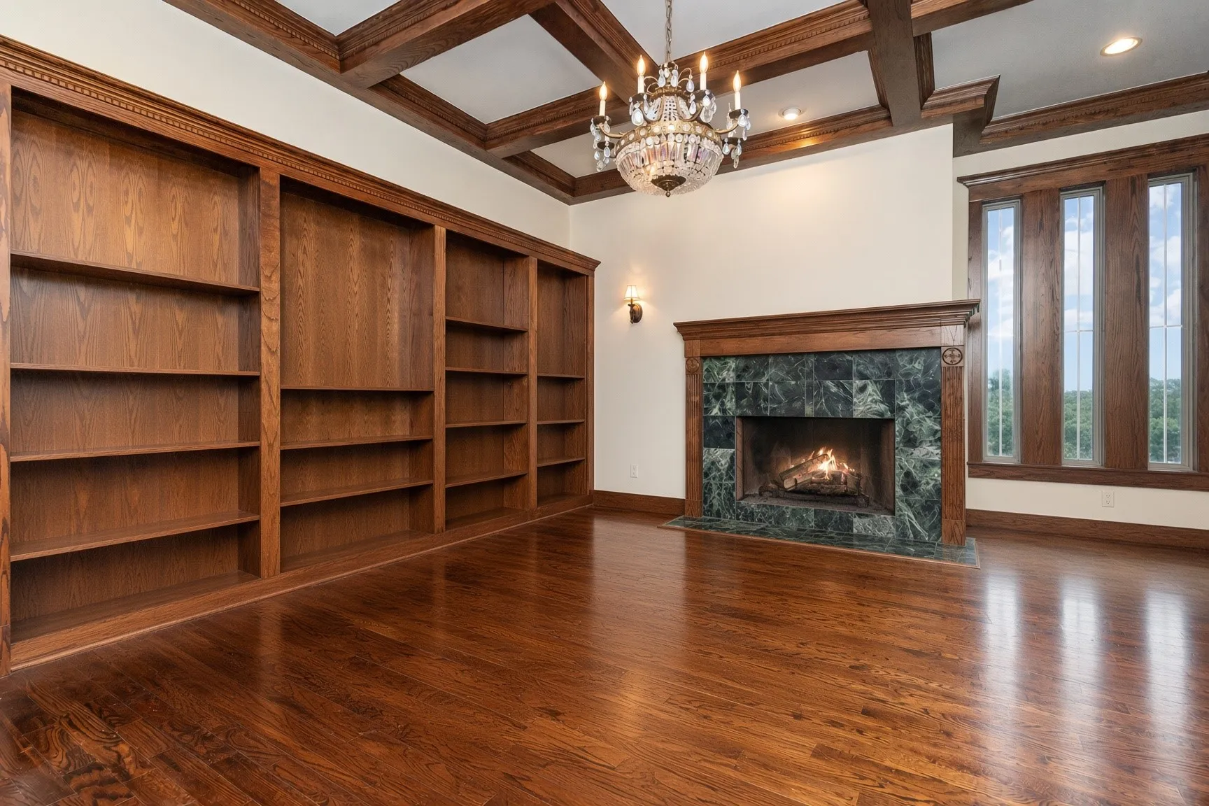 Hardwood flooring, built-in shelving, stone-faced fireplace with wood mantel, coffered ceiling, and chandelier