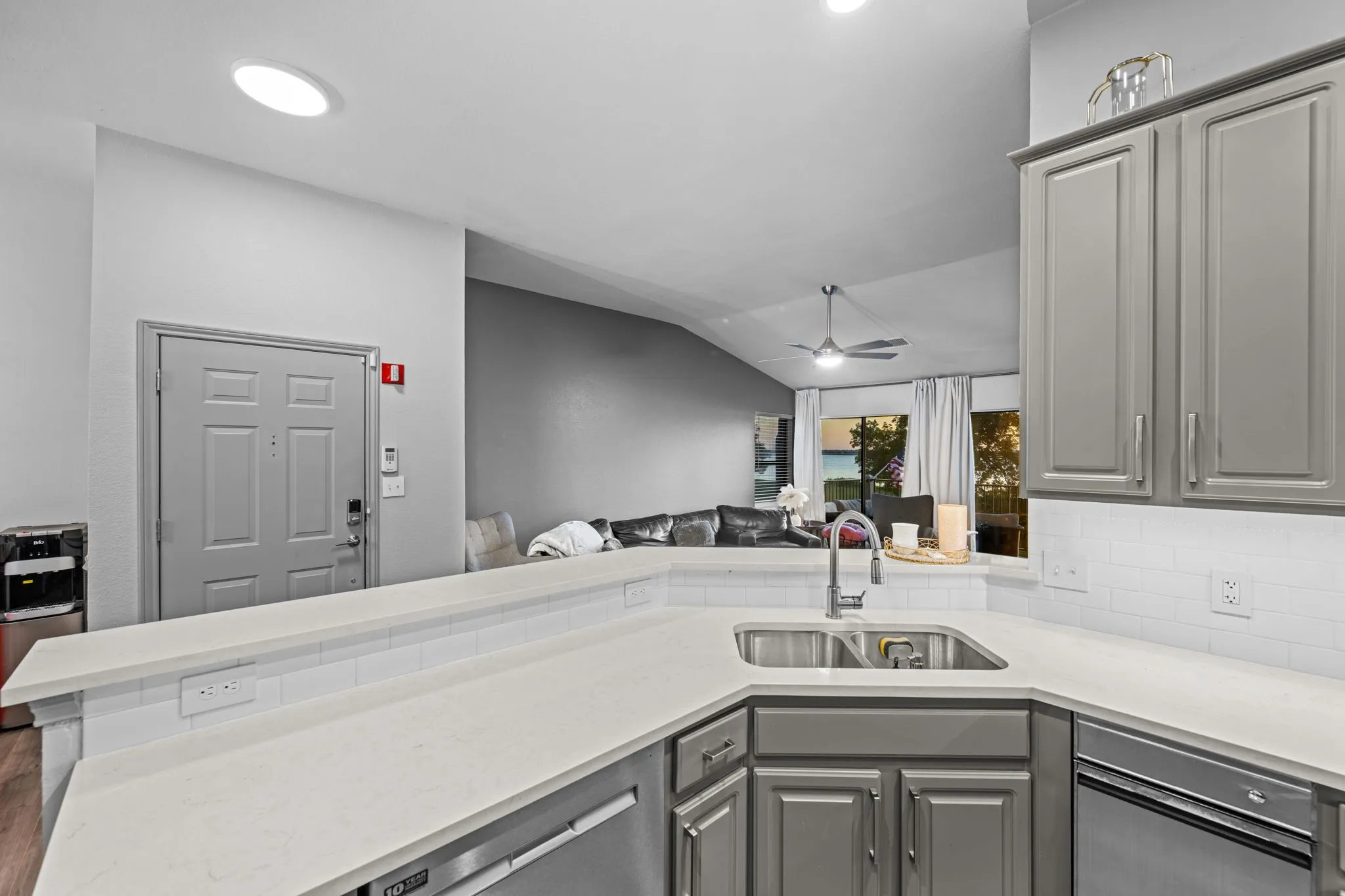 Kitchen featuring a double basin stainless steel sink, light gray cabinetry, white subway tile backsplash, and light-colored countertops