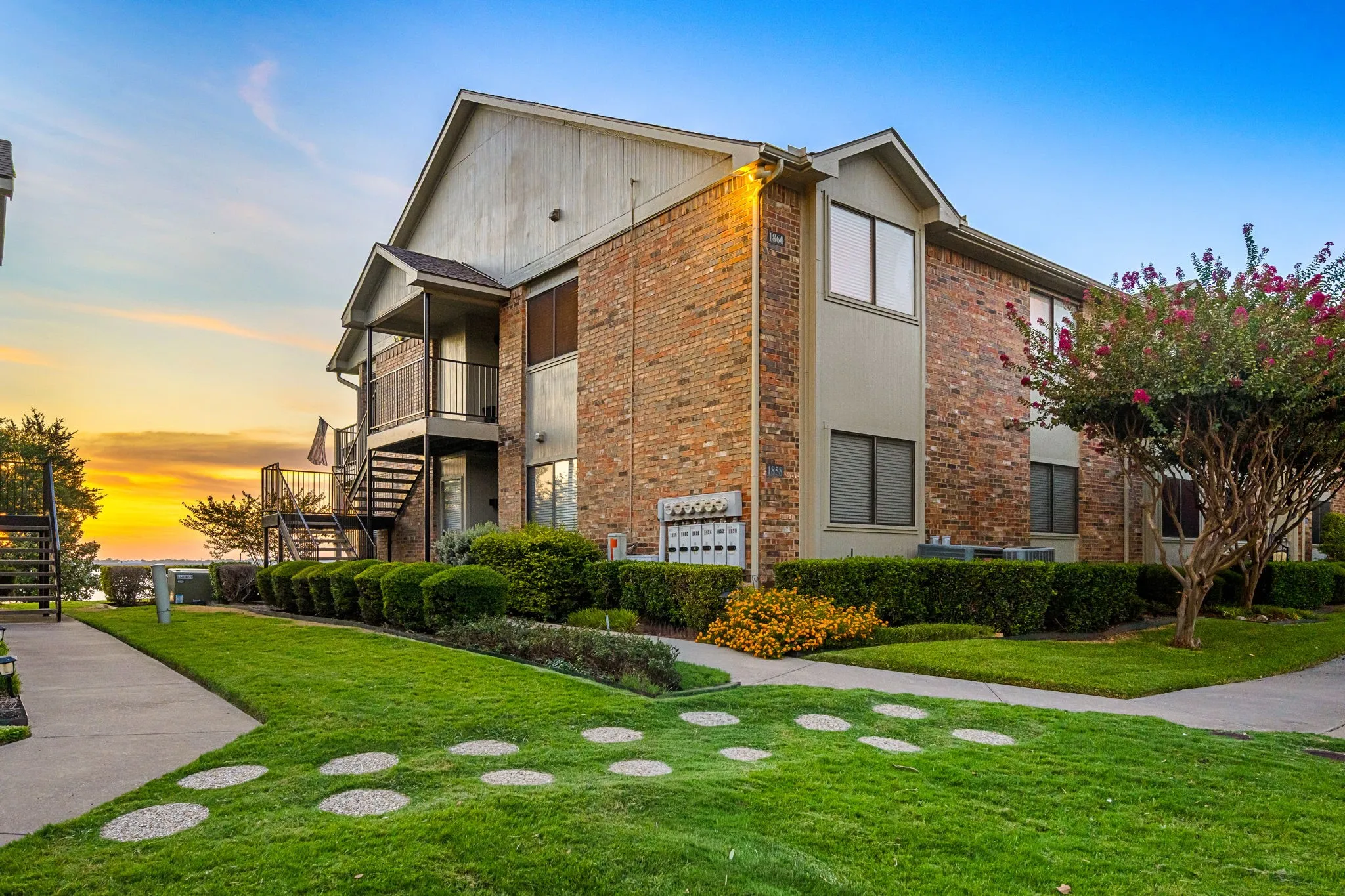 The building has a brick facade and sidewalk to the staircase that leads to the unit.