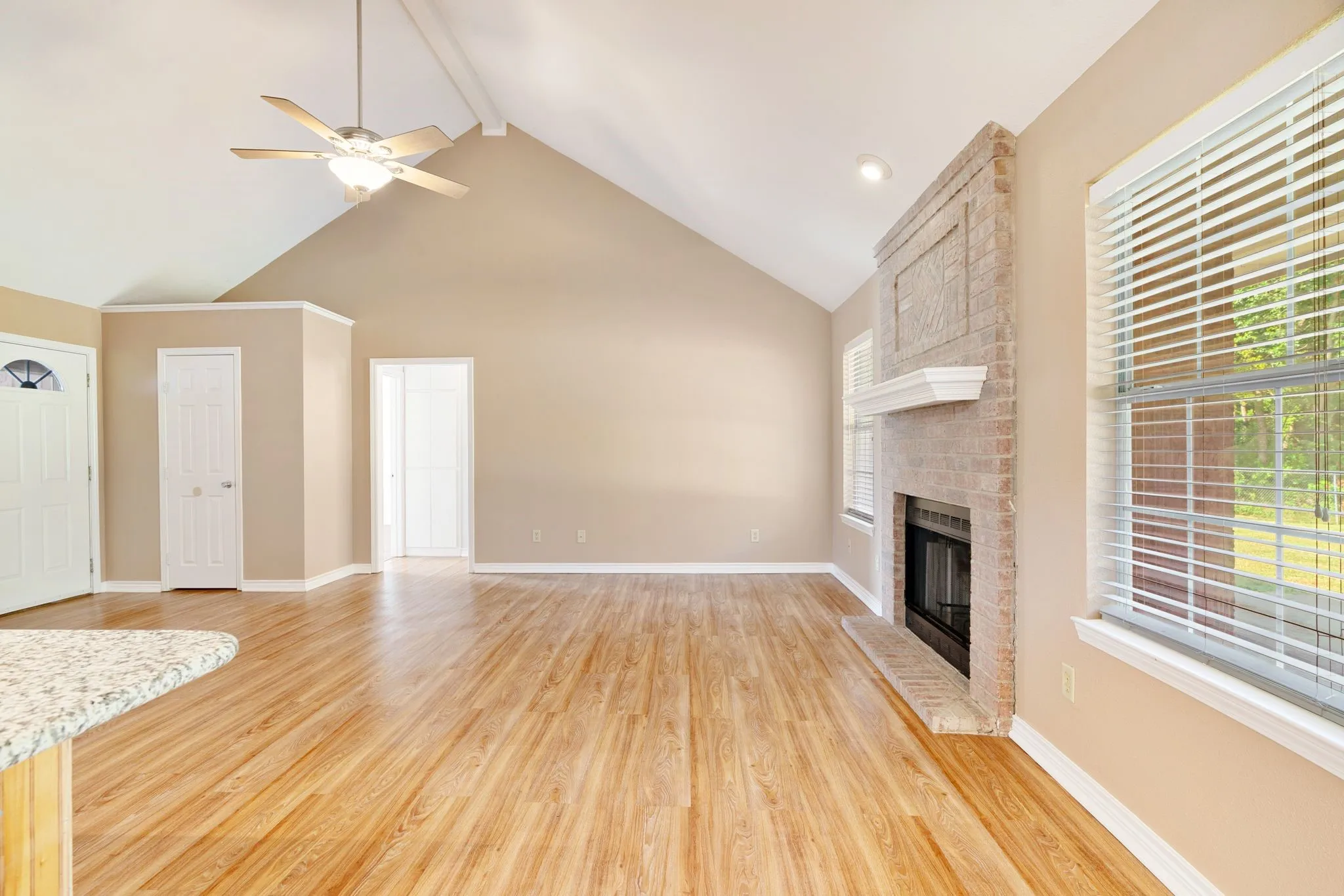 Vaulted ceiling with a ceiling fan, brick fireplace with a mantel, wood-finish flooring, recessed lighting, and a granite-finish countertop