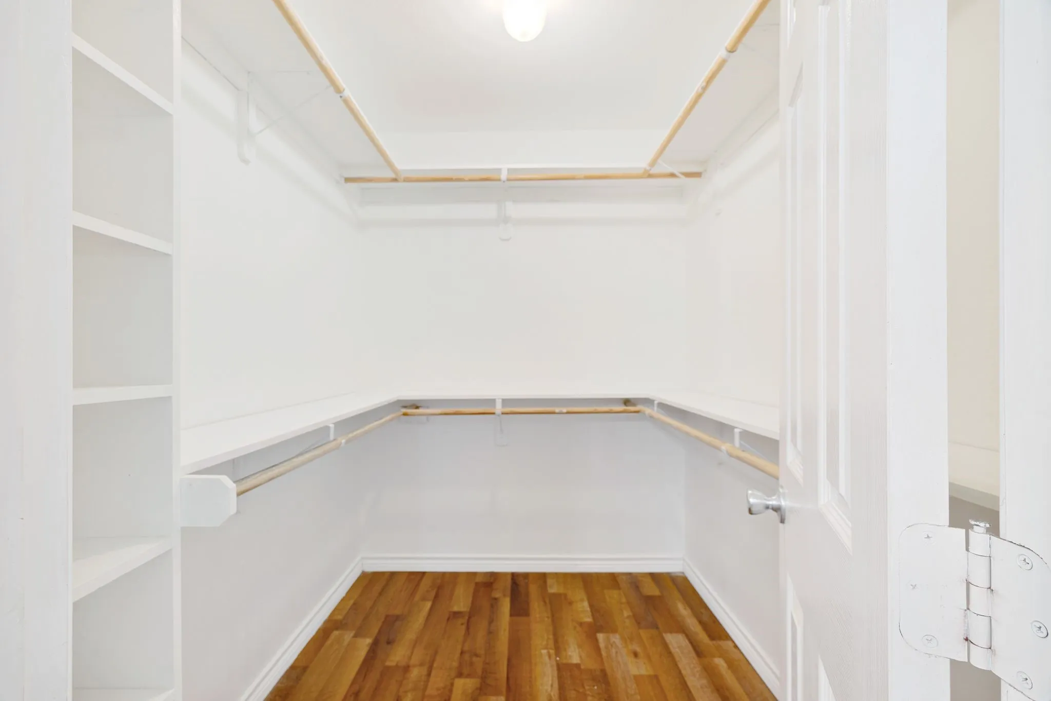 Walk-in closet featuring wood-finish flooring, built-in shelving, white walls, multiple hanging rods, and a ceiling-mounted light fixture