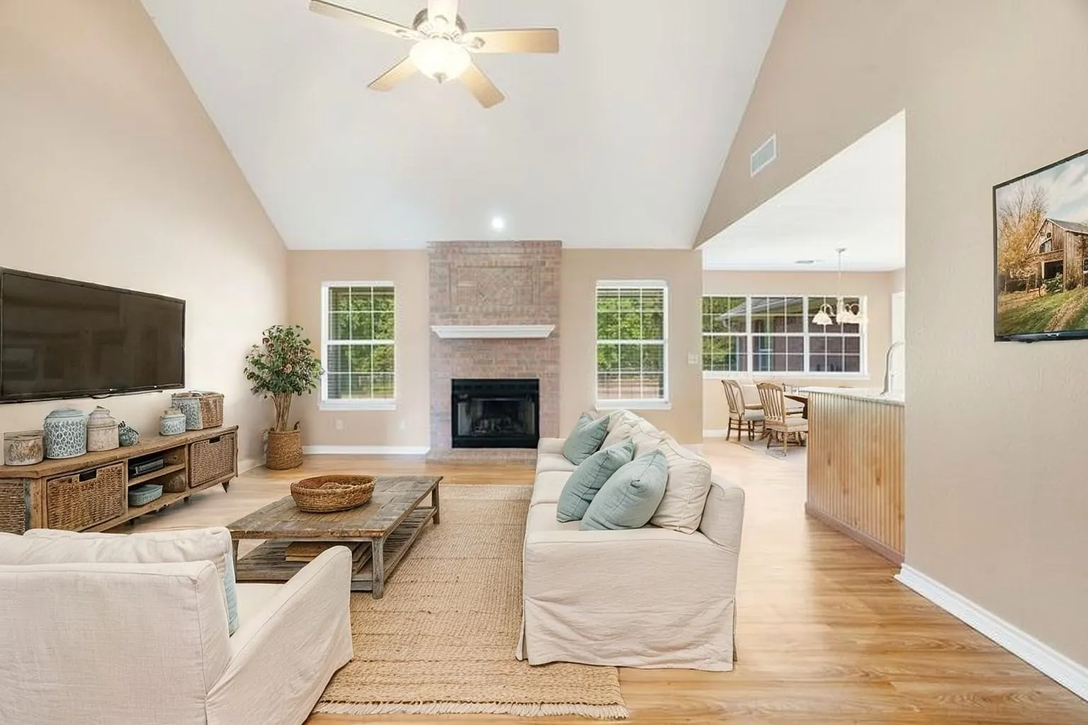 Vaulted ceilings with a ceiling fan, brick fireplace with mantel, multiple large windows, and wood-finish flooring