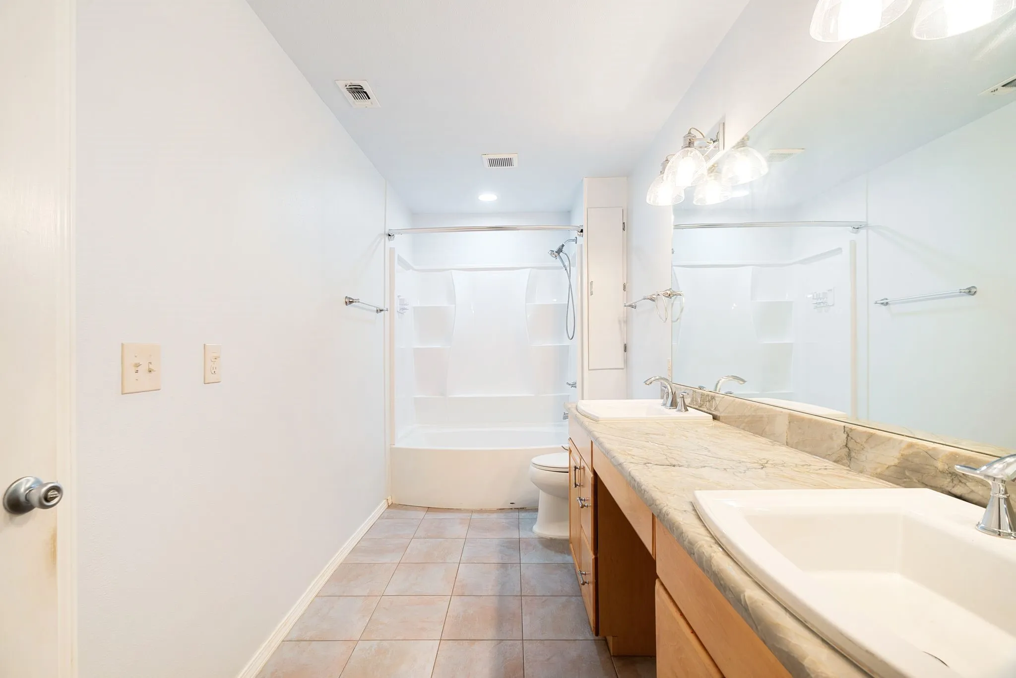 Double vanity with light wood cabinetry and a stone-finish countertop