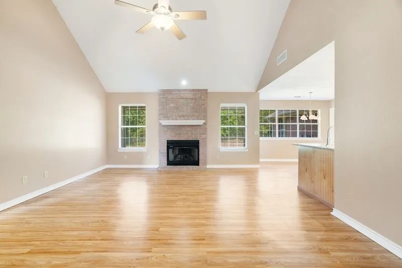 Spacious room featuring vaulted ceilings, wood-finish flooring, a brick fireplace with a white mantel, and multiple windows