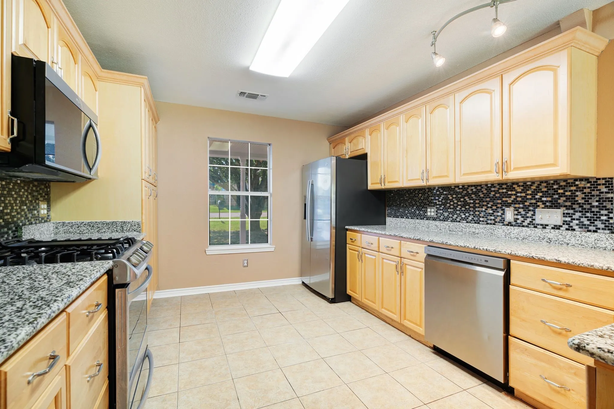 Kitchen featuring light wood cabinetry, granite-finish countertops, stainless steel appliances, and a mosaic tile backsplash