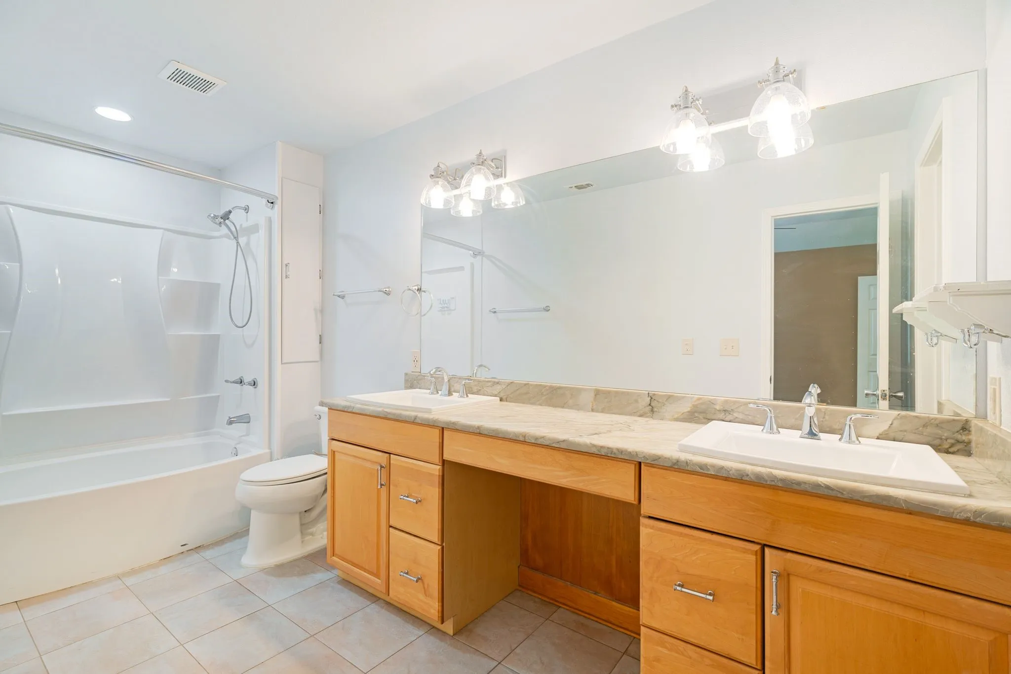 Full vanity with dual sinks, stone countertop, wood cabinetry, and an integrated mirror