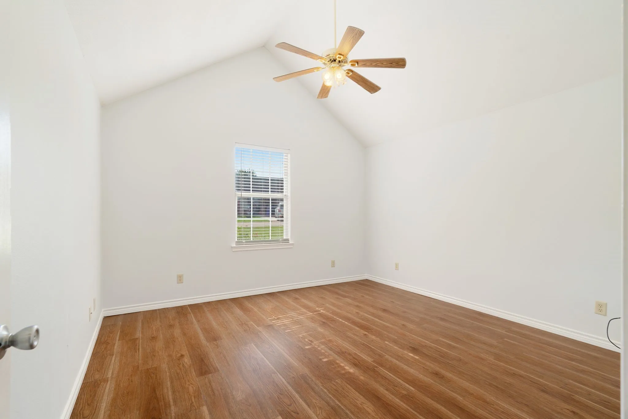 Room featuring a vaulted ceiling with a ceiling fan, wood-finish flooring, white baseboards, and a window with blinds