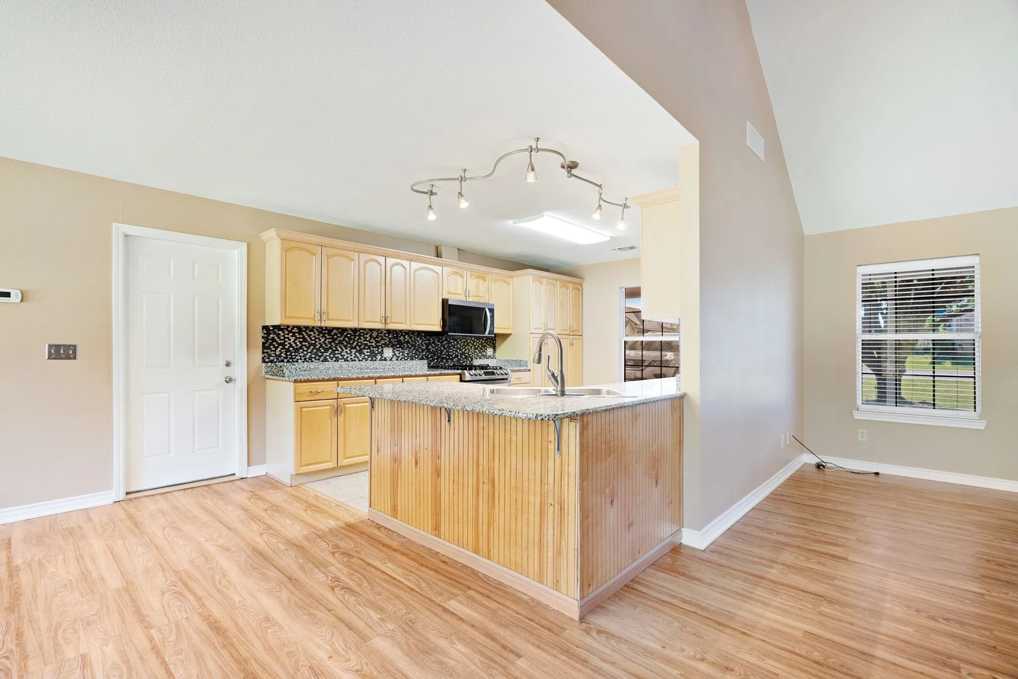 Kitchen featuring light wood cabinetry, a granite-style countertop island, and a black patterned backsplash