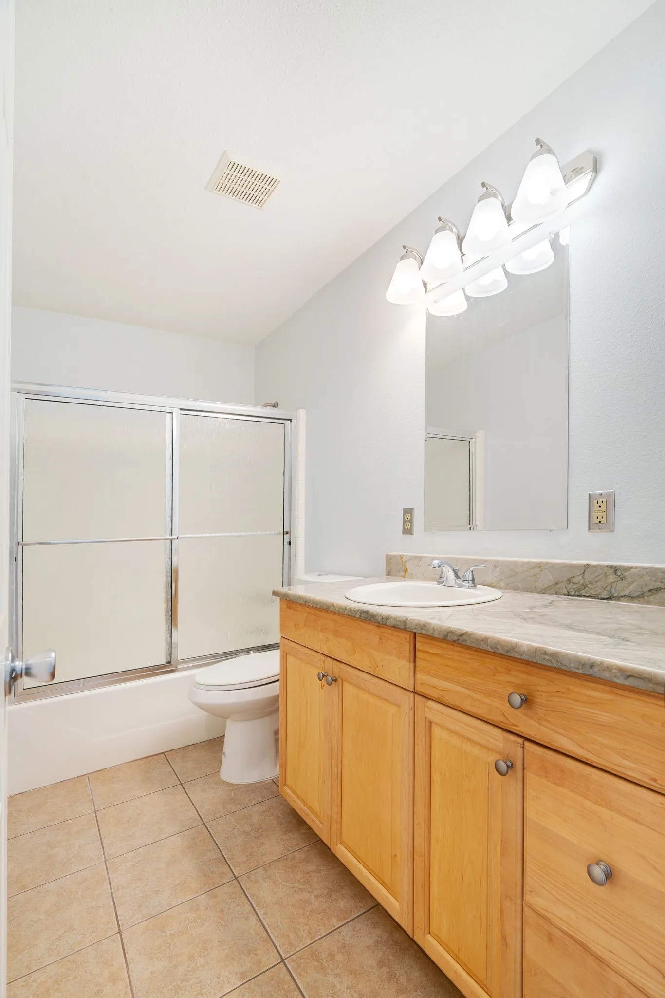 Bathroom featuring a light wood-finish vanity with a stone-finish countertop, single basin sink, and a four-light fixture