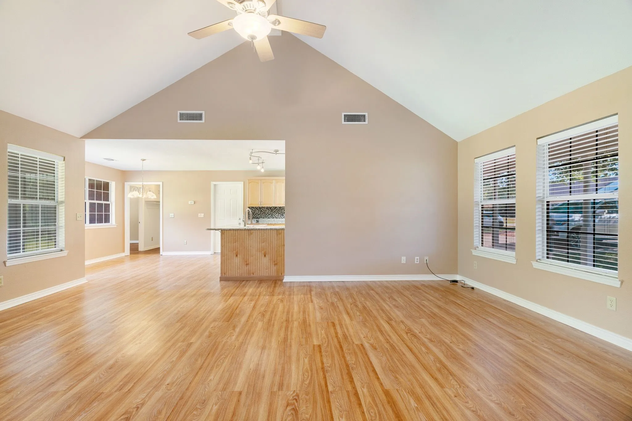Open concept living area featuring vaulted ceilings, wood-finish flooring, multiple windows with blinds, and a ceiling fan