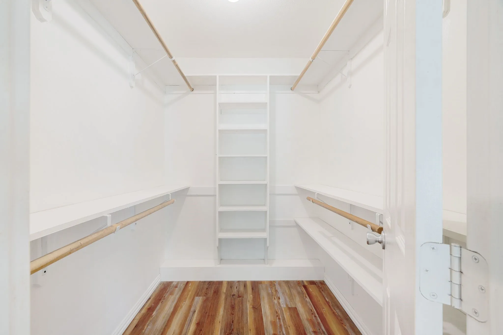 Walk-in closet featuring bright white walls, wood-finish flooring, built-in shelving, and dual hanging rods