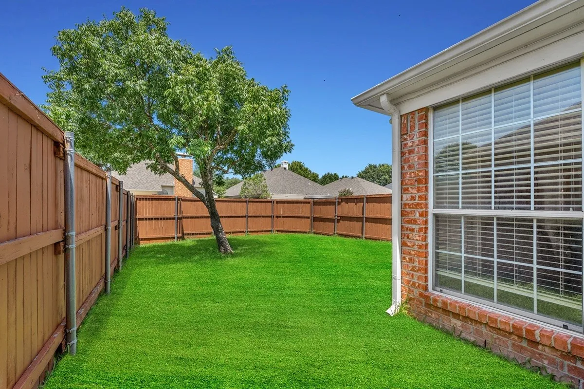 Expansive backyard featuring a lush green lawn, mature shade tree, and wood privacy fencing
