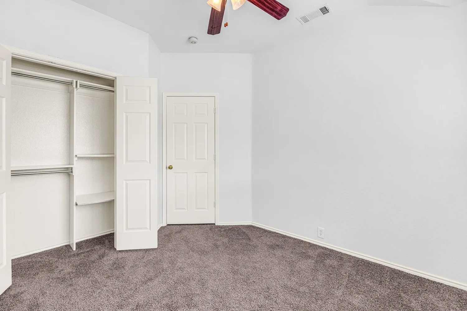 Room featuring neutral-toned carpet, white walls, a ceiling fan with integrated lighting, and a bi-fold door closet with shelving and hanging rods