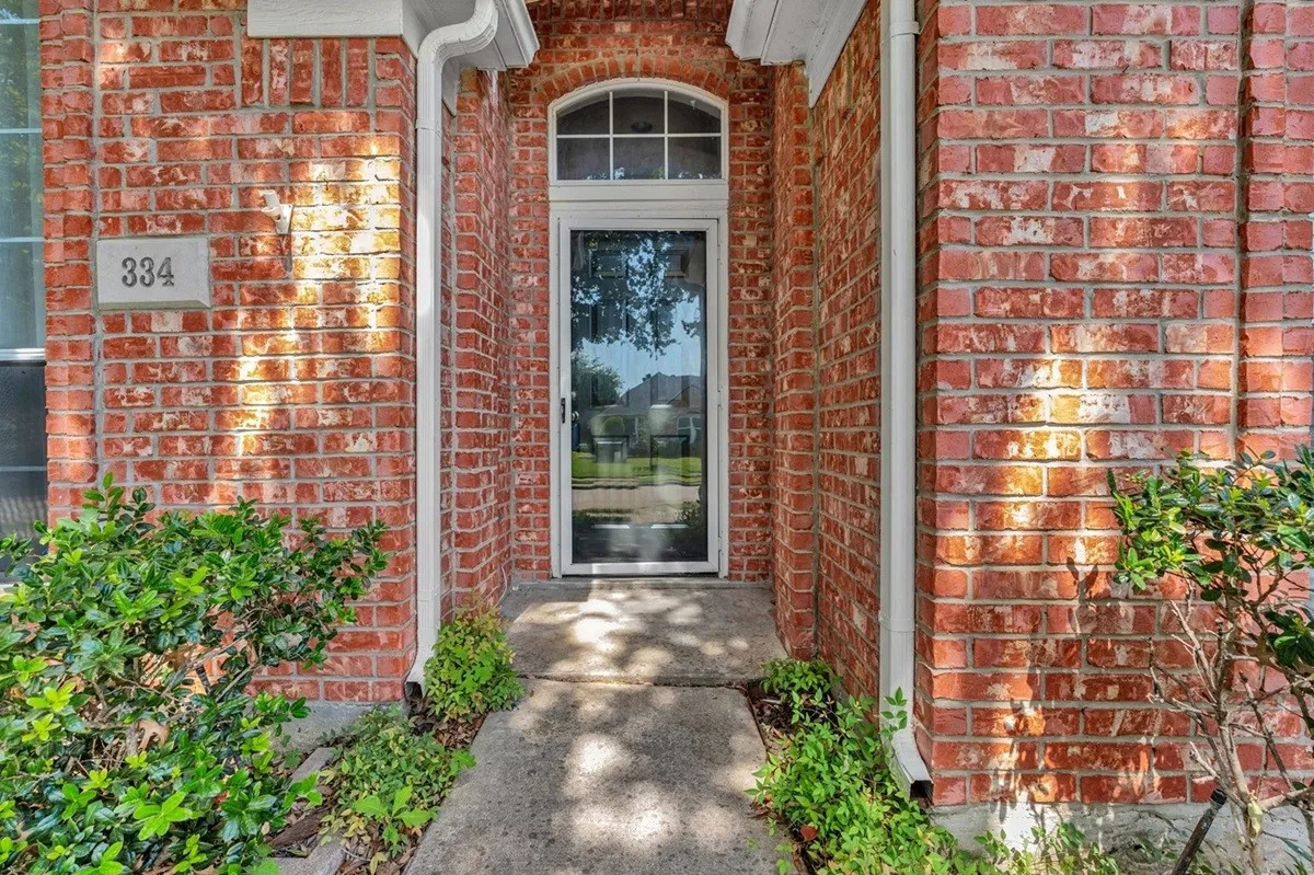 Red brick exterior with white trim accents and a concrete pathway leading to the arched entry door