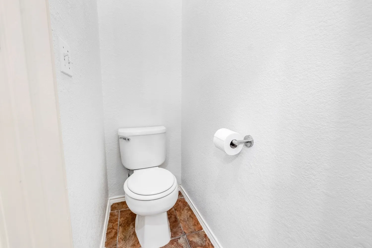 White toilet fixture with a polished chrome flush lever, set against textured white walls and brown-toned floor tiling