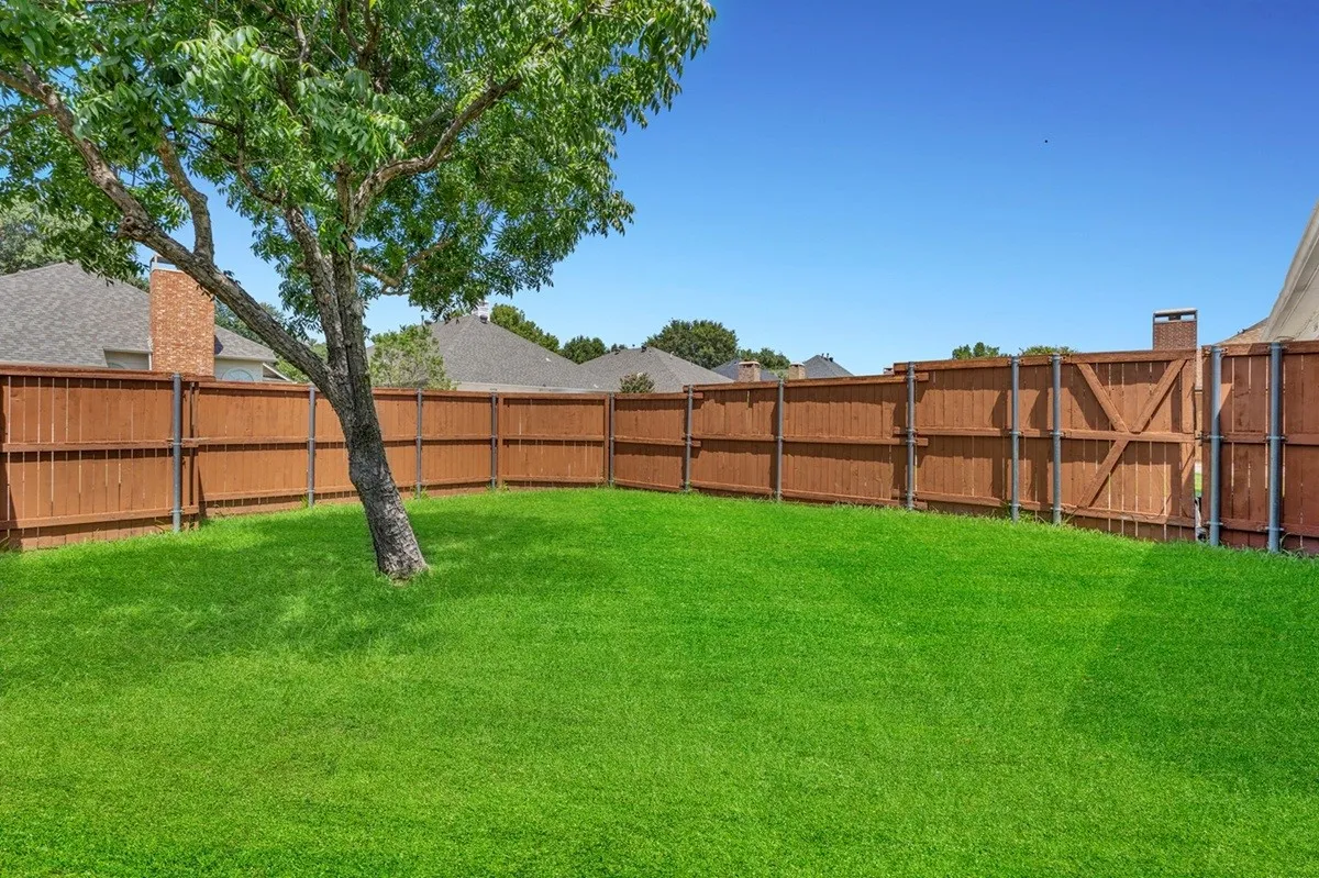 Expansive backyard featuring a manicured lawn, established tree, and full privacy fencing with a gate