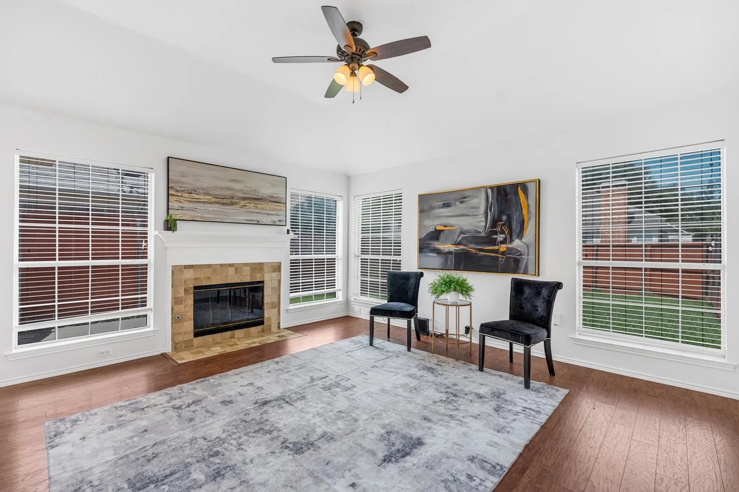 Living area featuring warm wood-finish flooring, a ceiling fan with integrated lighting, and multiple windows with white blinds