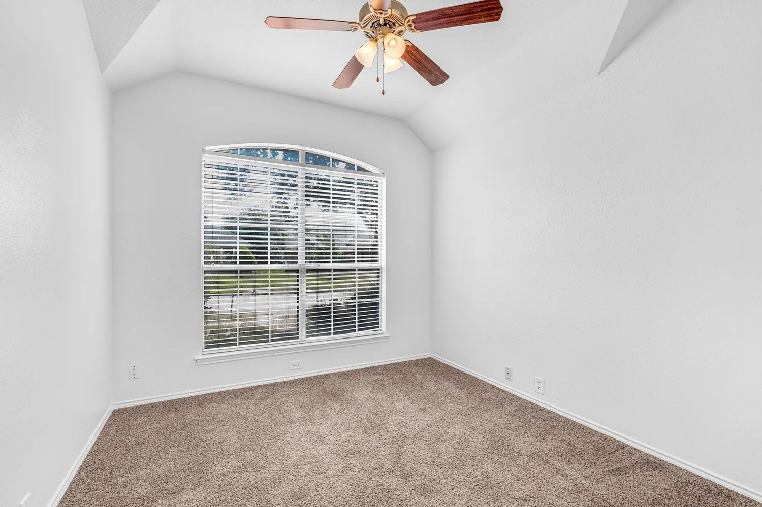 Arched window with blinds, vaulted ceiling, ceiling fan with light kit, textured walls, and neutral carpet flooring