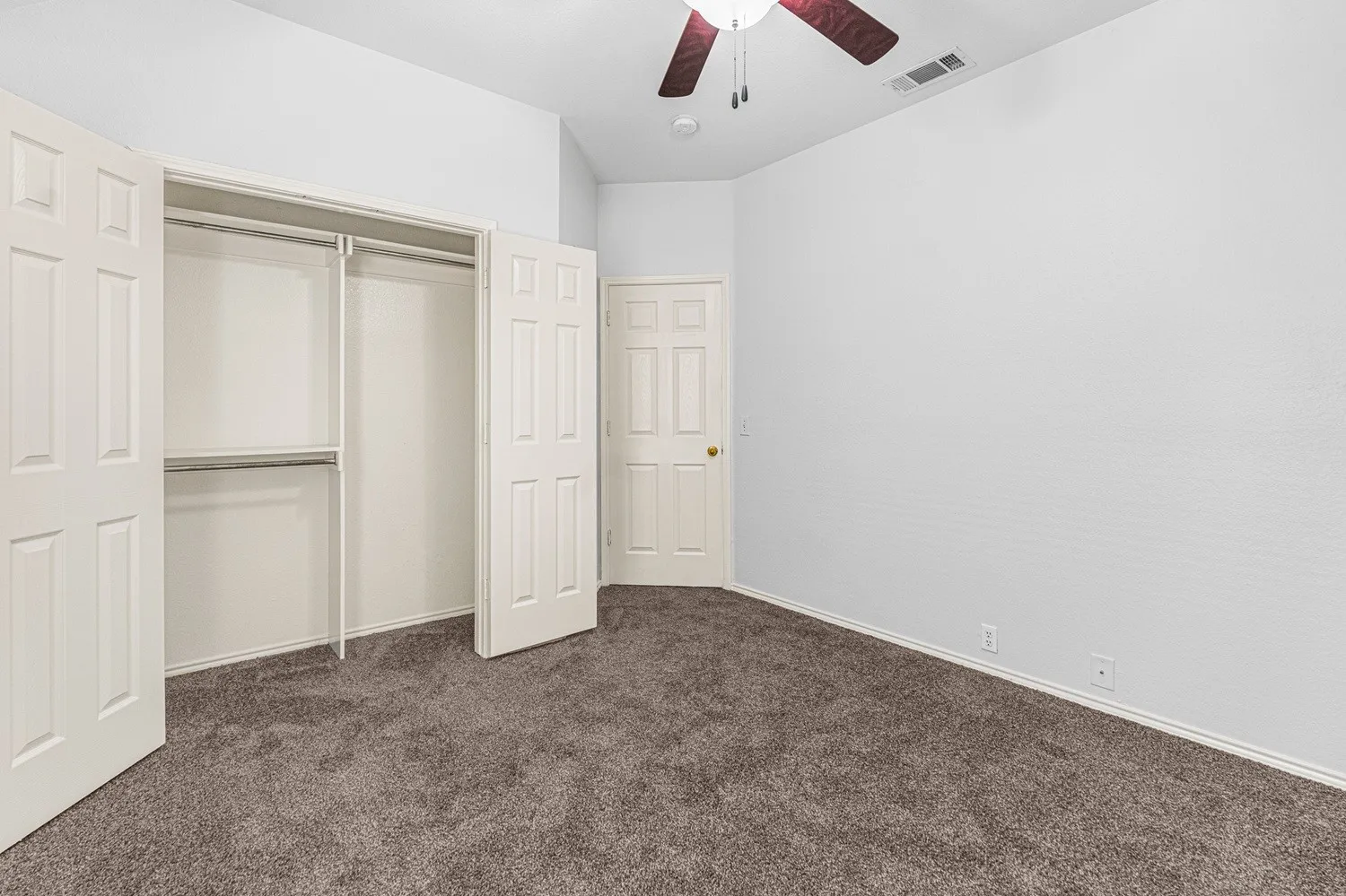 Bedroom featuring plush gray carpeting, a ceiling fan with dark wood-finish blades, and a double-door closet with shelving and hanging rods