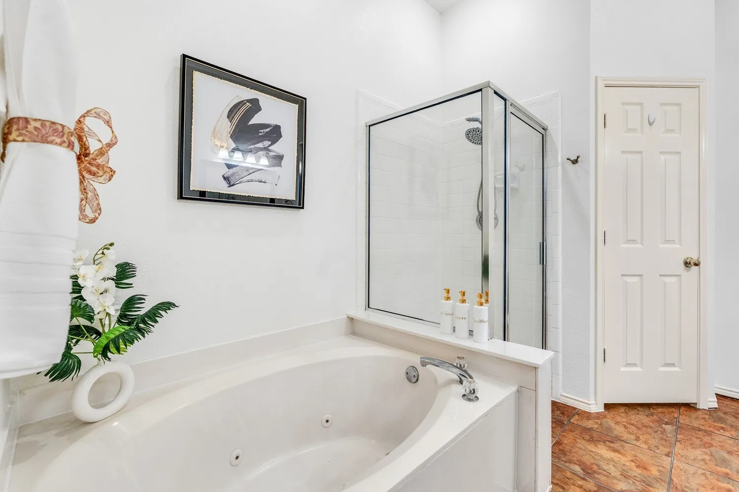 Built-in jetted tub with polished chrome fixtures, glass-enclosed shower with tile surround, white paneled door, and textured flooring