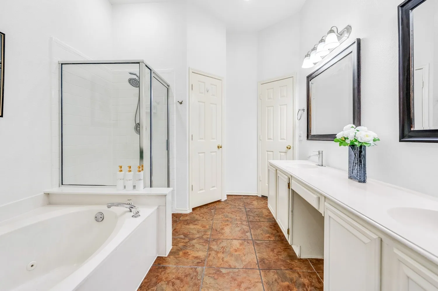 Bathroom featuring a white built-in soaking tub, glass-enclosed shower, dual vanity with undermount sinks, and stone-finish tile flooring