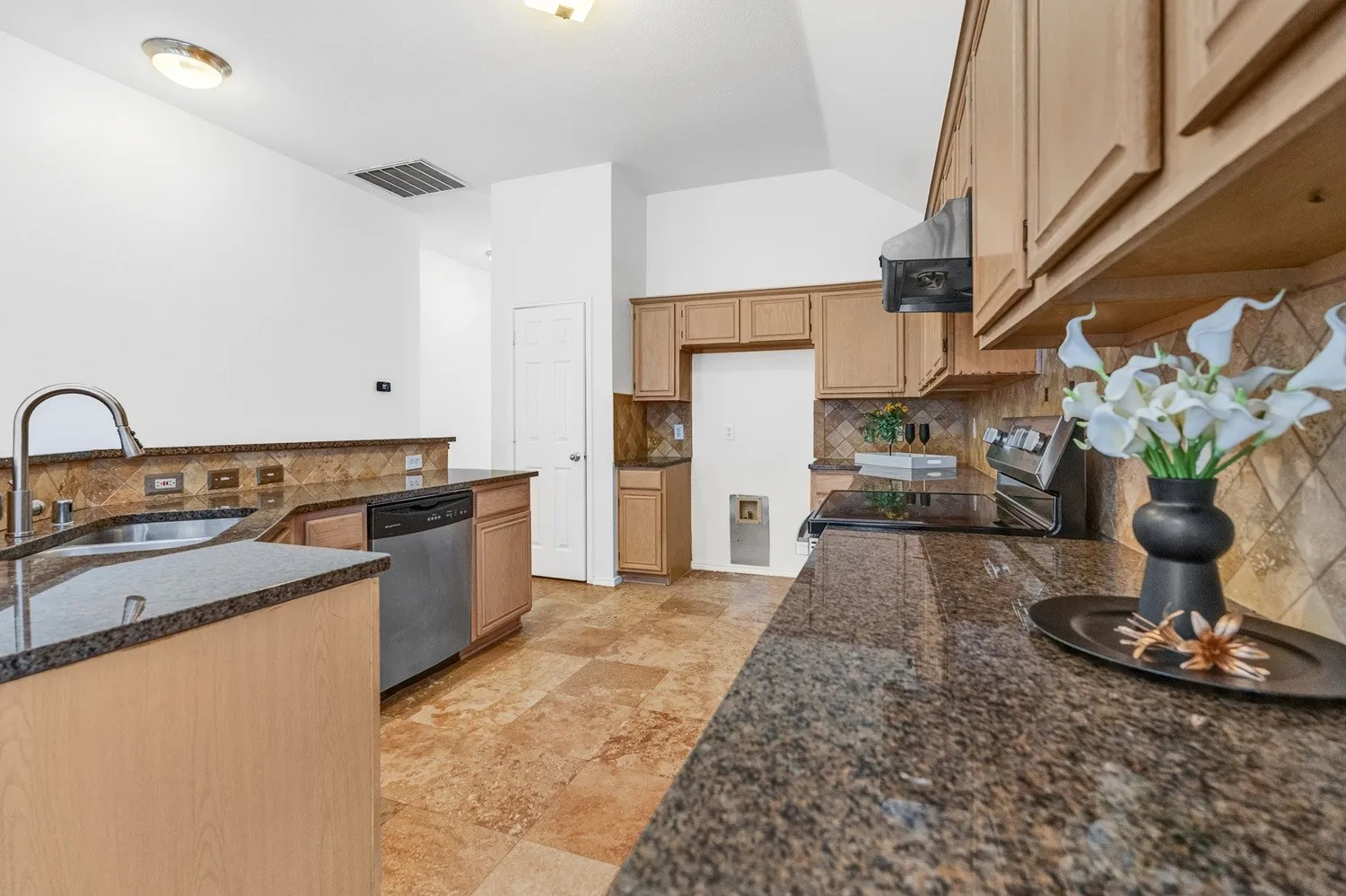 Kitchen featuring granite countertops, wood cabinetry, stainless steel dishwasher, and a tile backsplash
