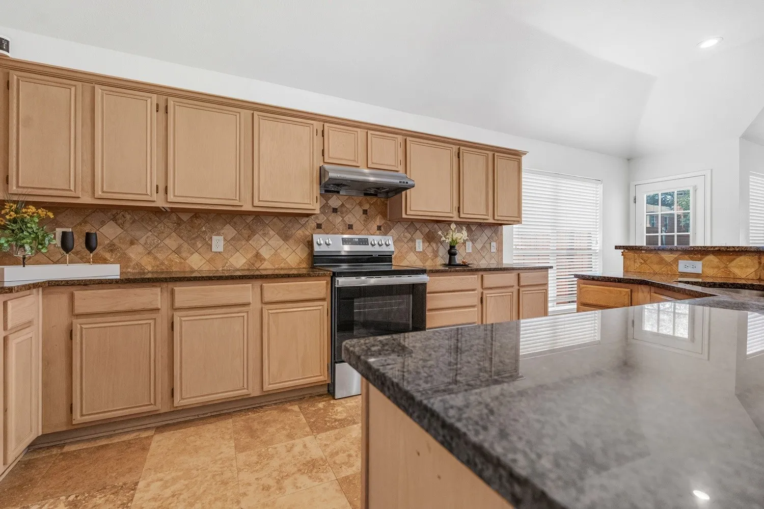 Kitchen featuring light wood cabinetry, granite countertops, a tile backsplash, and stainless steel appliances
