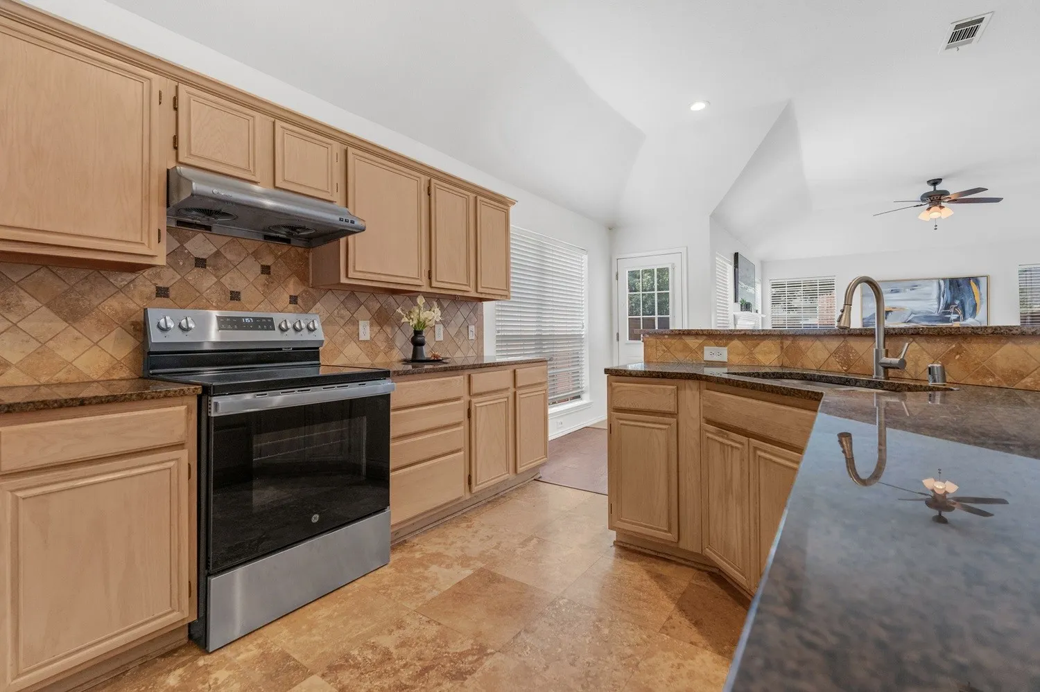 Kitchen featuring light wood cabinetry, stone countertops, stainless steel electric range, stone tile backsplash, and tile flooring