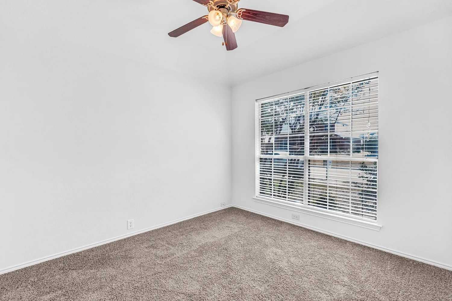 Carpeted room featuring a ceiling fan with light fixture, a large window with blinds, and white baseboards