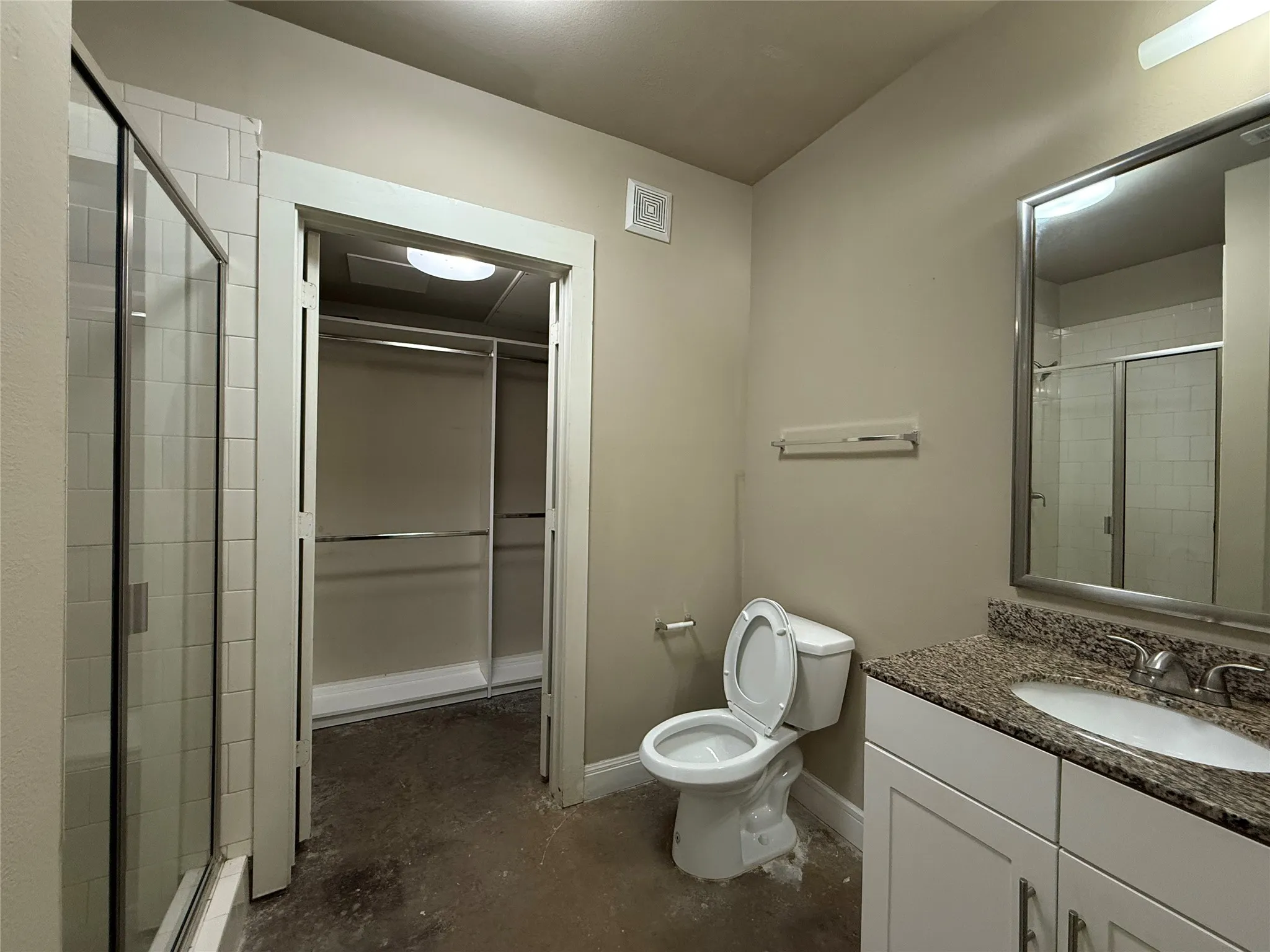 Bathroom featuring a glass-enclosed shower with subway tile surround, a vanity with a granite-style countertop and undermount sink, a framed mirror, and a water closet
