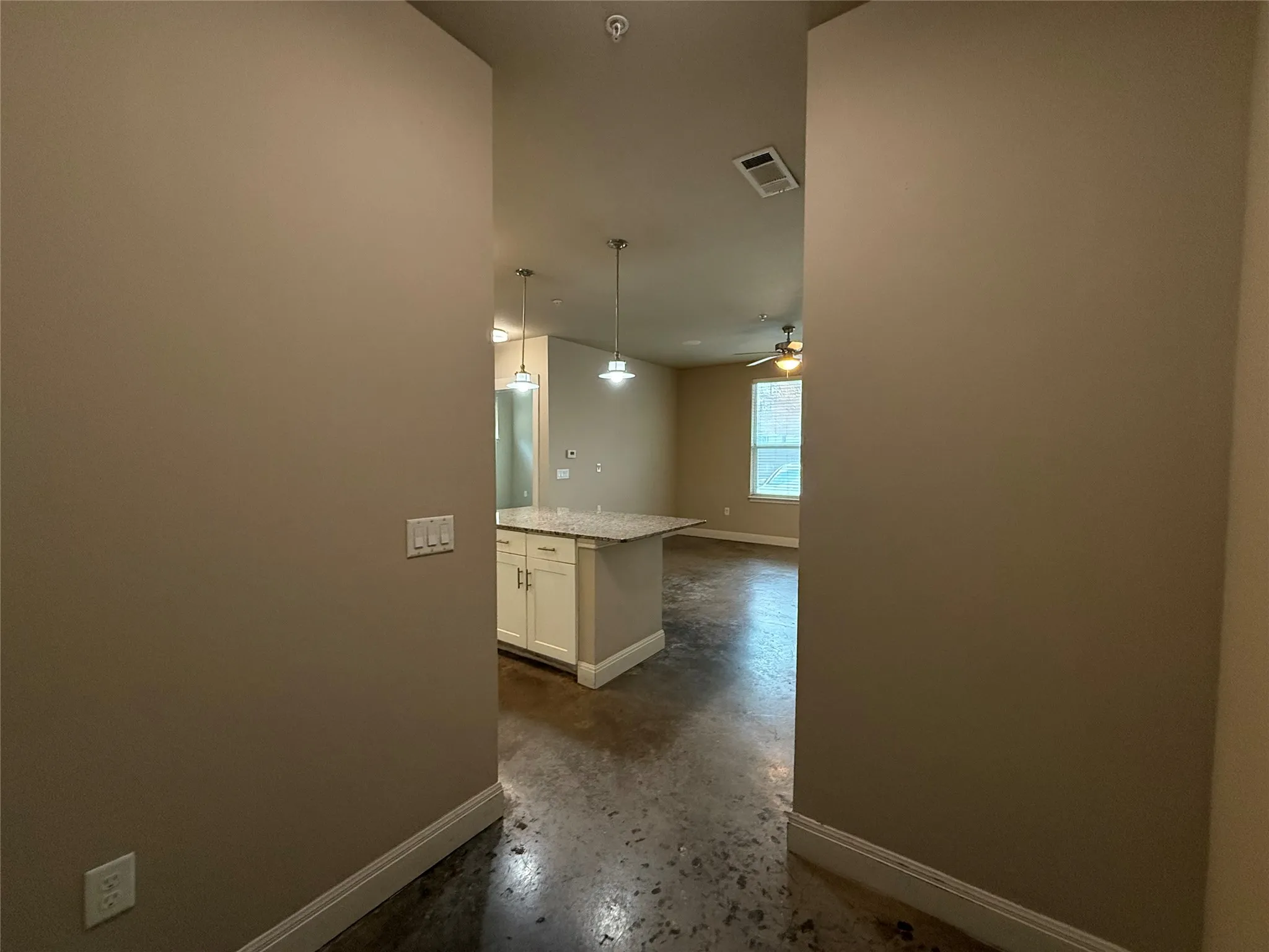 Open-concept living area featuring concrete-finish flooring, a kitchen island with stone countertop, and pendant lighting