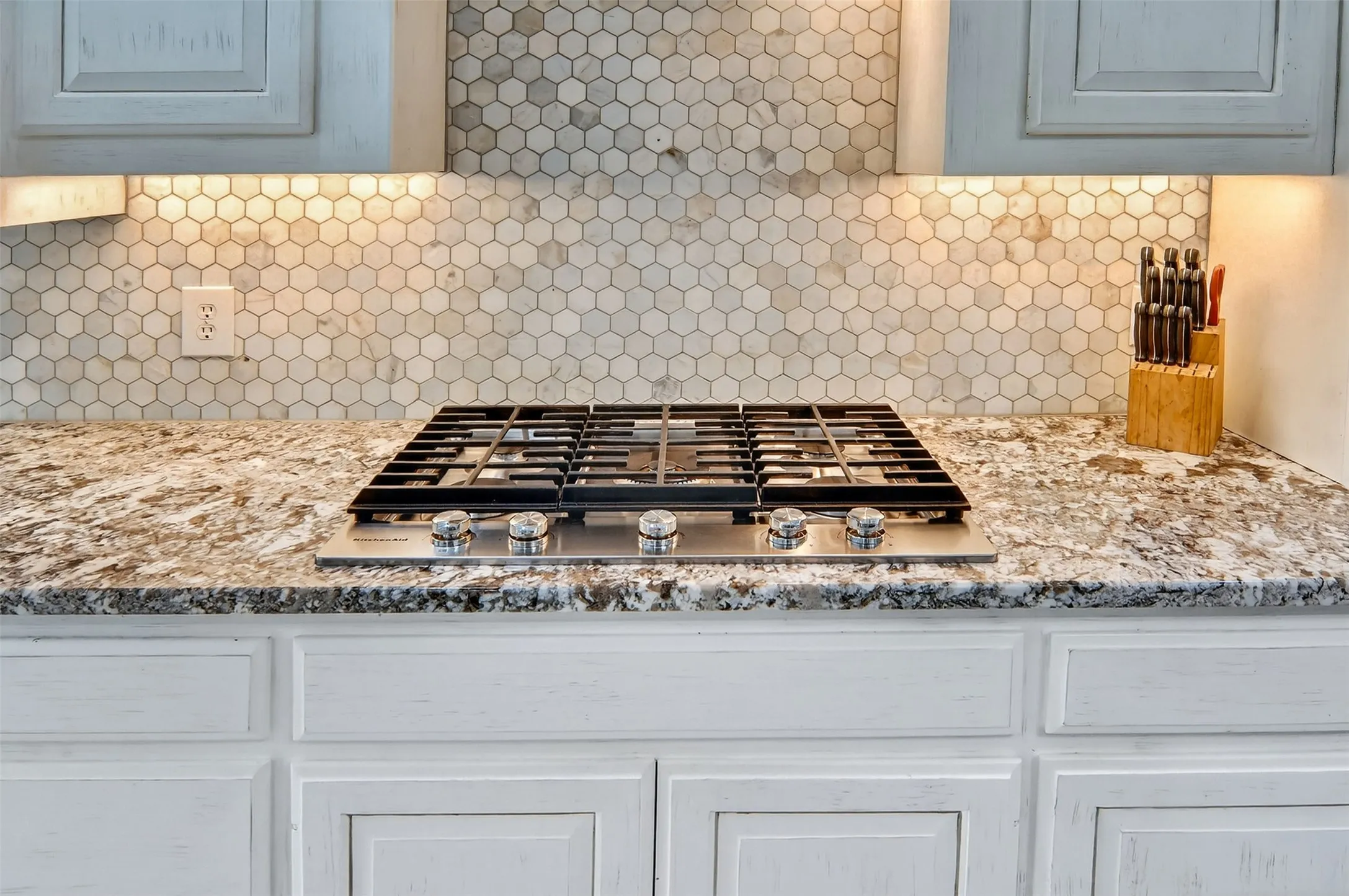 Five burner gas cooktop, granite counters, tile backsplash, and under cabinet lighting.